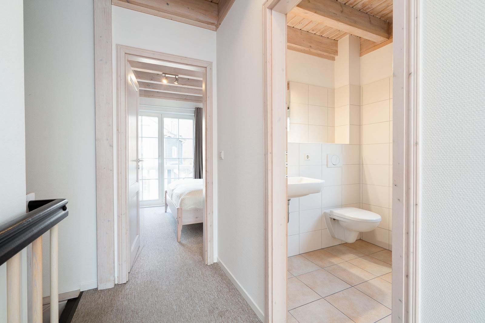 Hallway with bedroom and bathroom. Wooden beams and white walls.