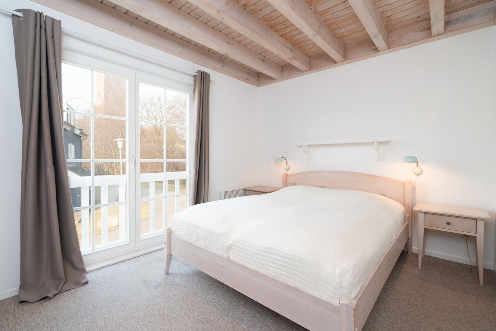Bedroom with wooden beam ceiling, bed, nightstand, and window to terrace.