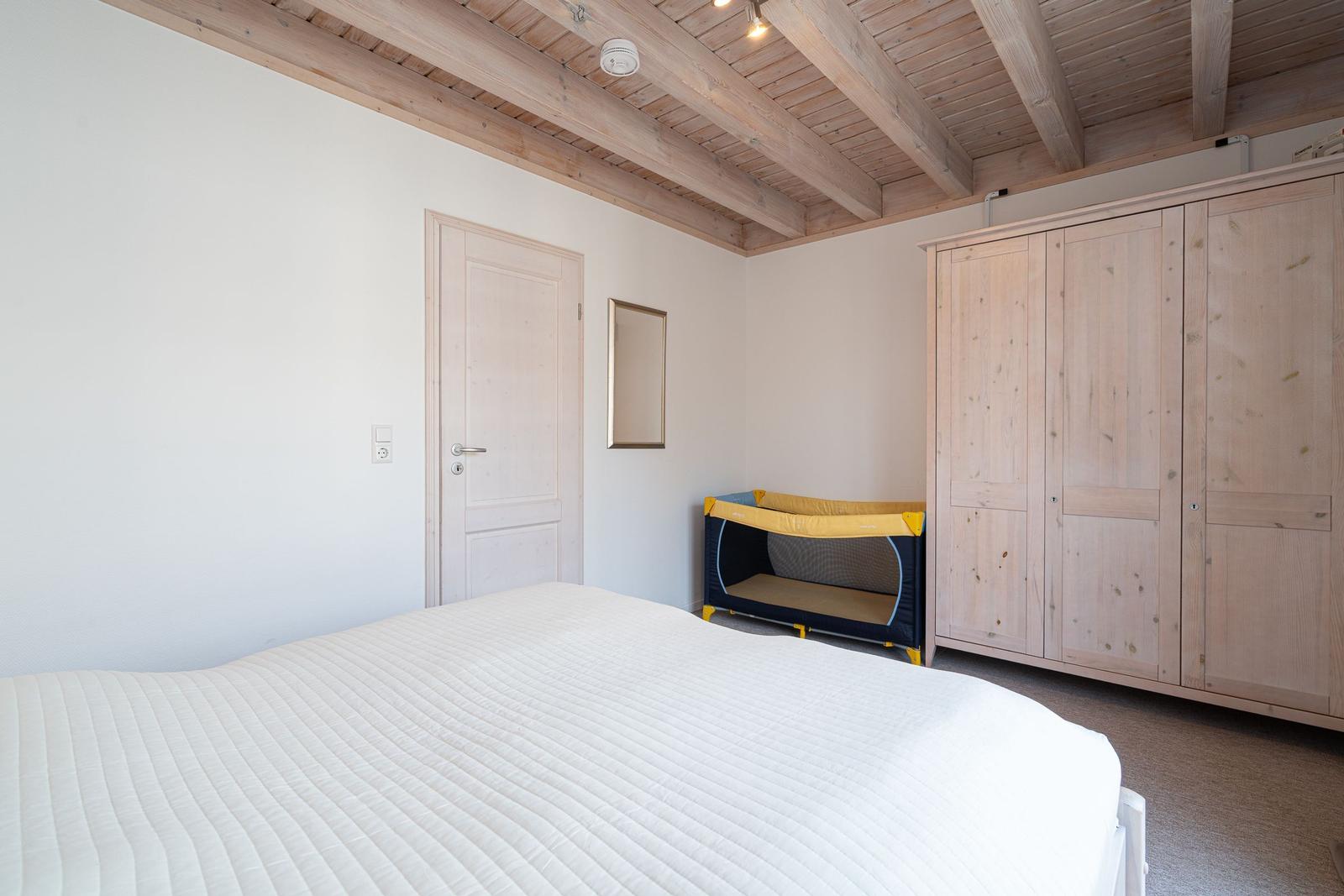 Bedroom with bed, wardrobe, and baby crib under wooden beam ceiling.