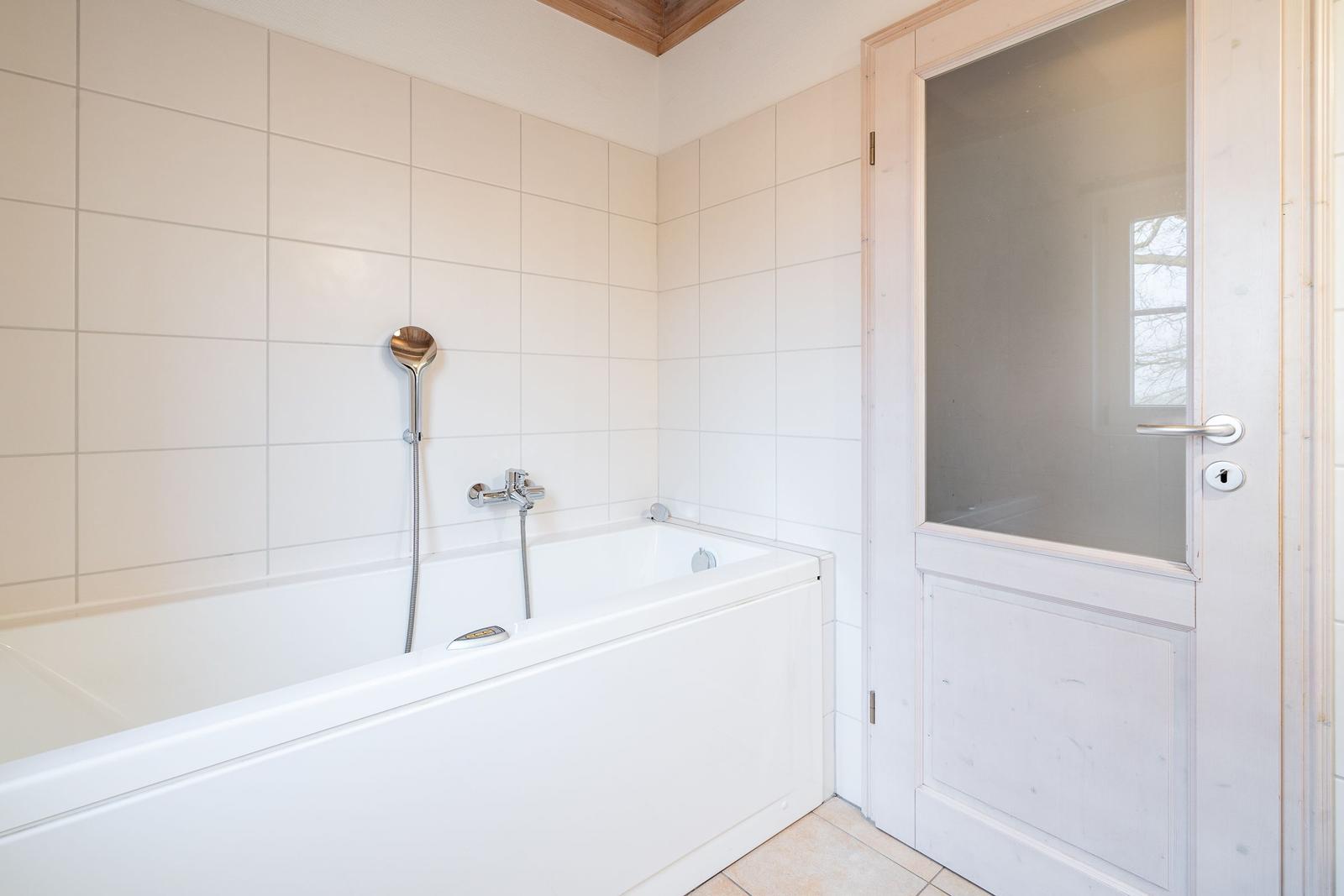 Bath with bathtub, showerhead, and wooden door