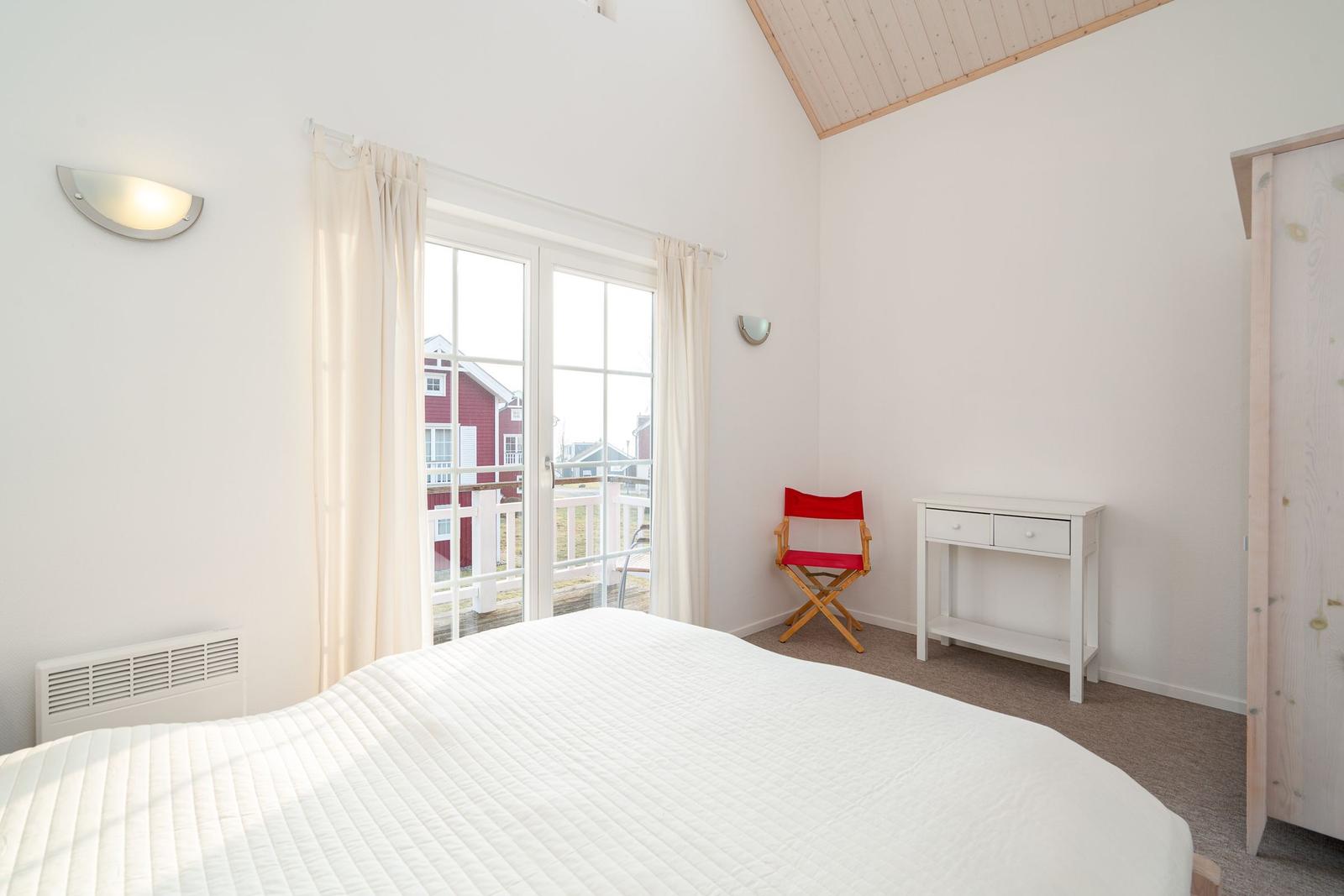 Bedroom with white bed, window, and red chair.