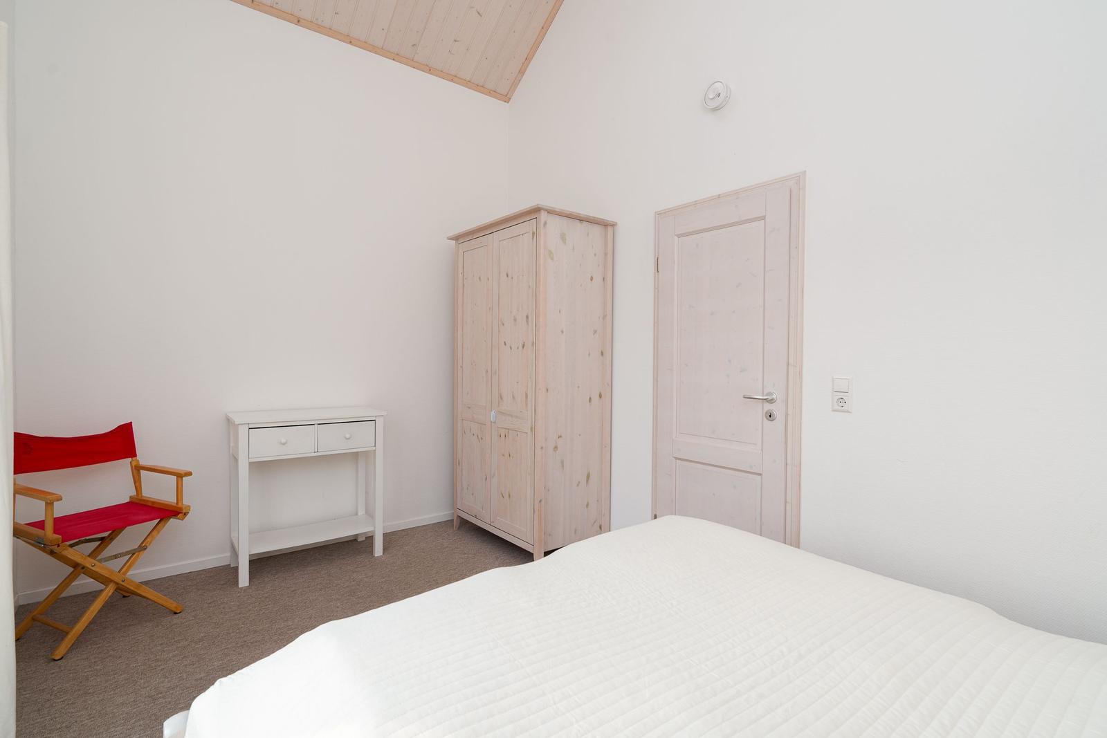 Bedroom with bed, wardrobe, desk, and red chair.