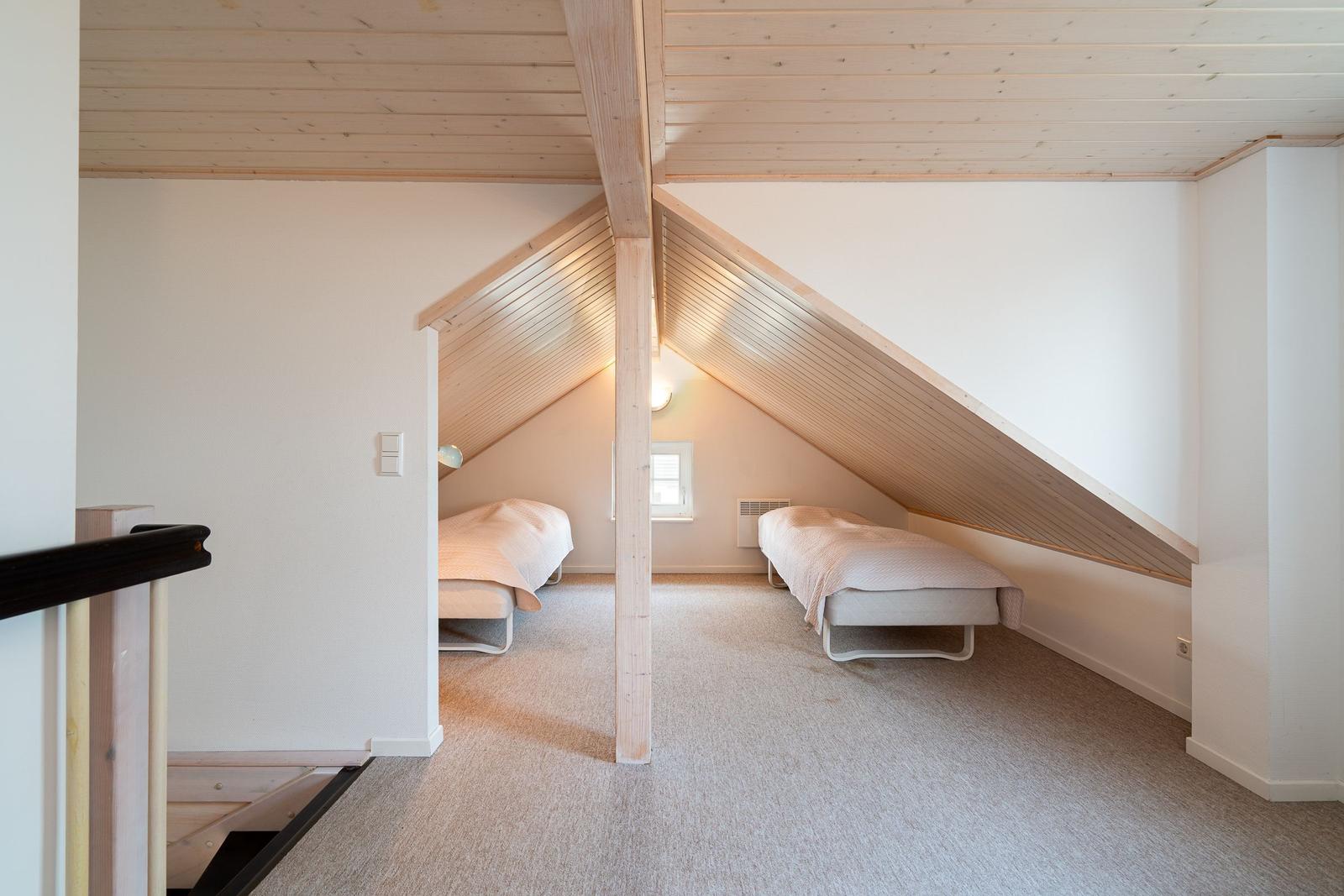 Two beds in an attic room with wooden ceiling and window.