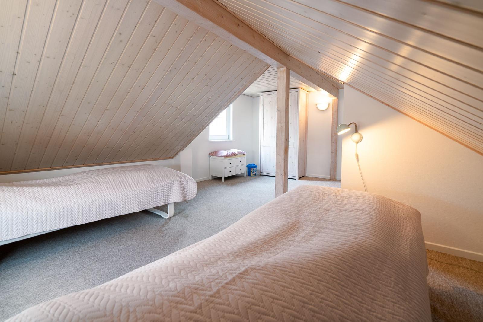 Room with two beds, wooden ceiling, and closet in background.