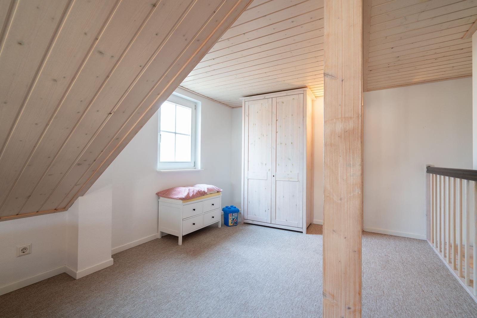 Attic room with wooden ceiling, wardrobe, and window.