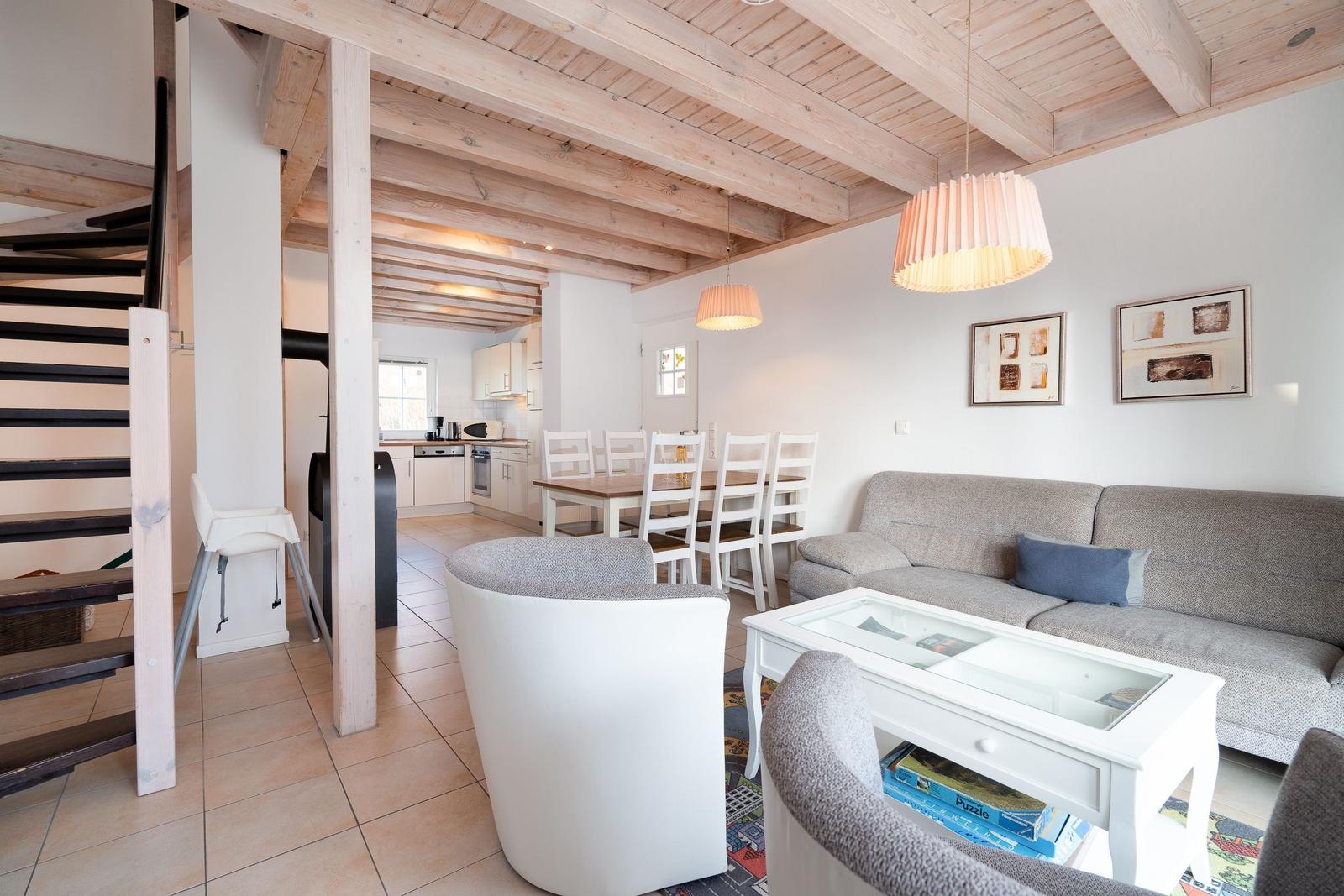 Living area with sofa, dining table, and kitchen under wooden beams.