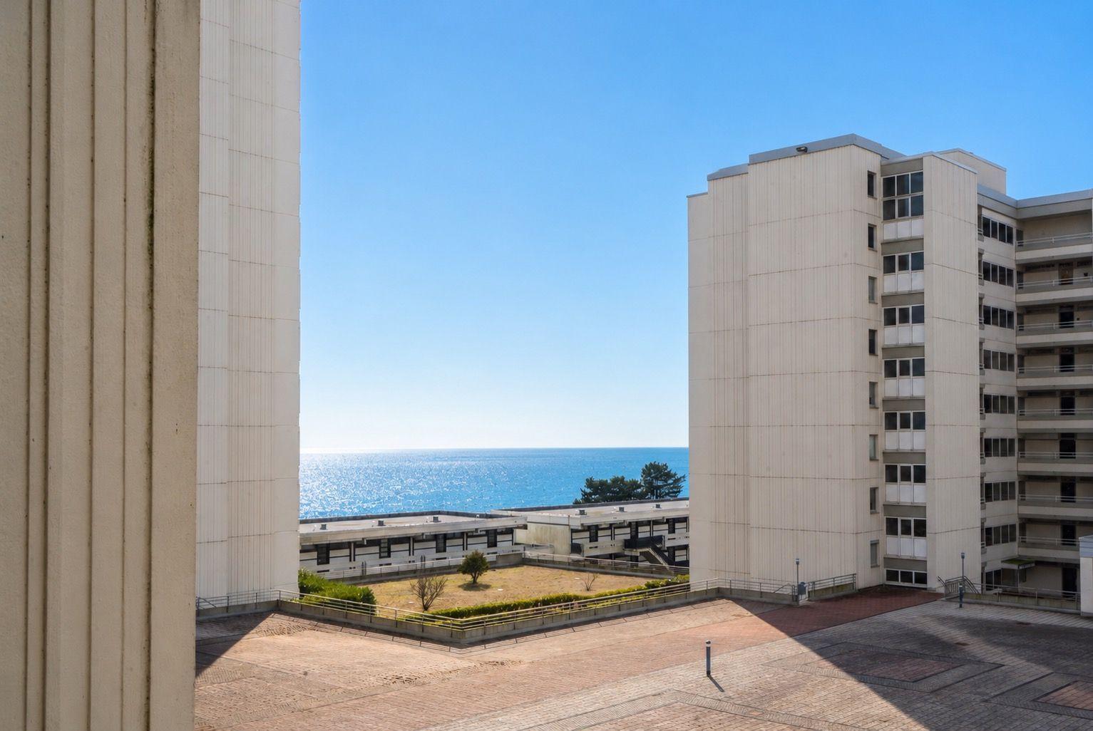 Ausblick auf das Meer zwischen zwei Hochhäusern mit gepflastertem Platz und Grünflächen.
