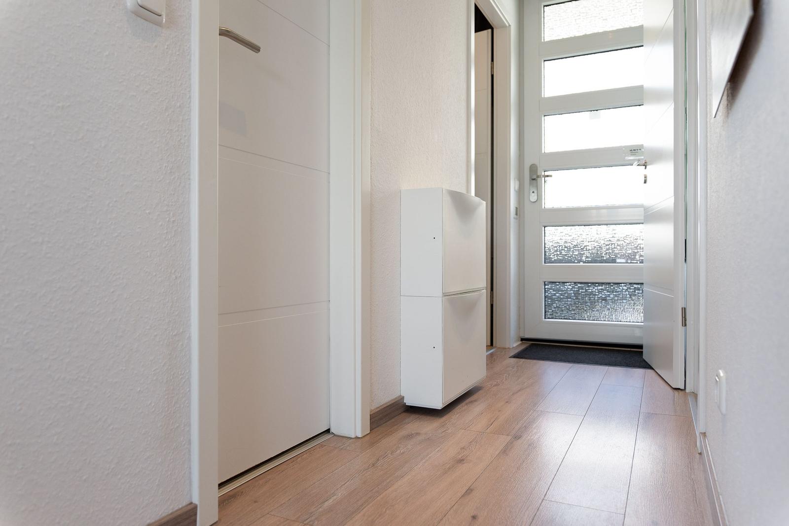 Eingangsbereich mit Holzboden, weißen Wänden und Schuhschrank neben der Tür.