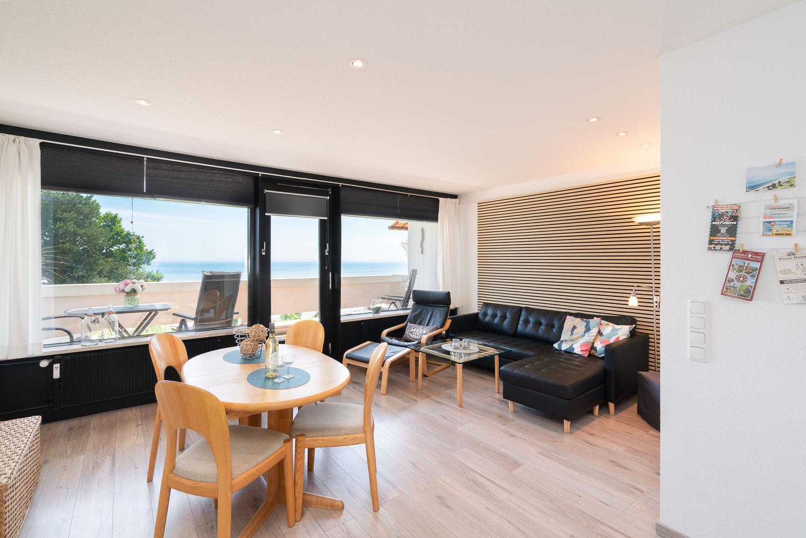 Wohn- und Essbereich mit Blick aufs Meer. Holzboden, schwarze Couch und Essgruppe.