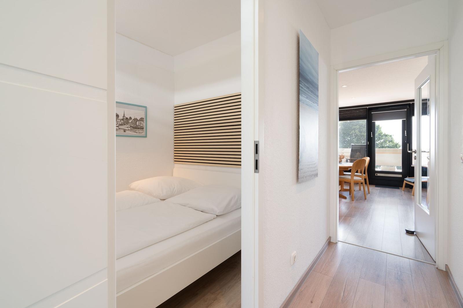 Schlafzimmer mit Bett und Wandbild. Durchgang zur Küche mit Tisch und Stühlen.