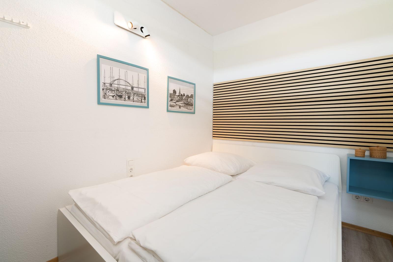 Ein Schlafzimmer mit weißem Bett, Holzpaneelen an der Wand und zwei Bildern an der Wand.