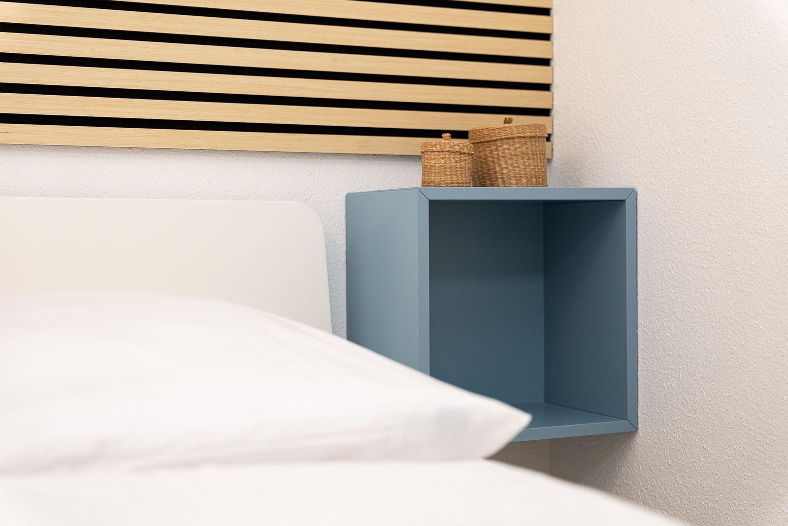 Schlafzimmer mit Bett, blauem Nachttisch und Holzpaneelen an der Wand.