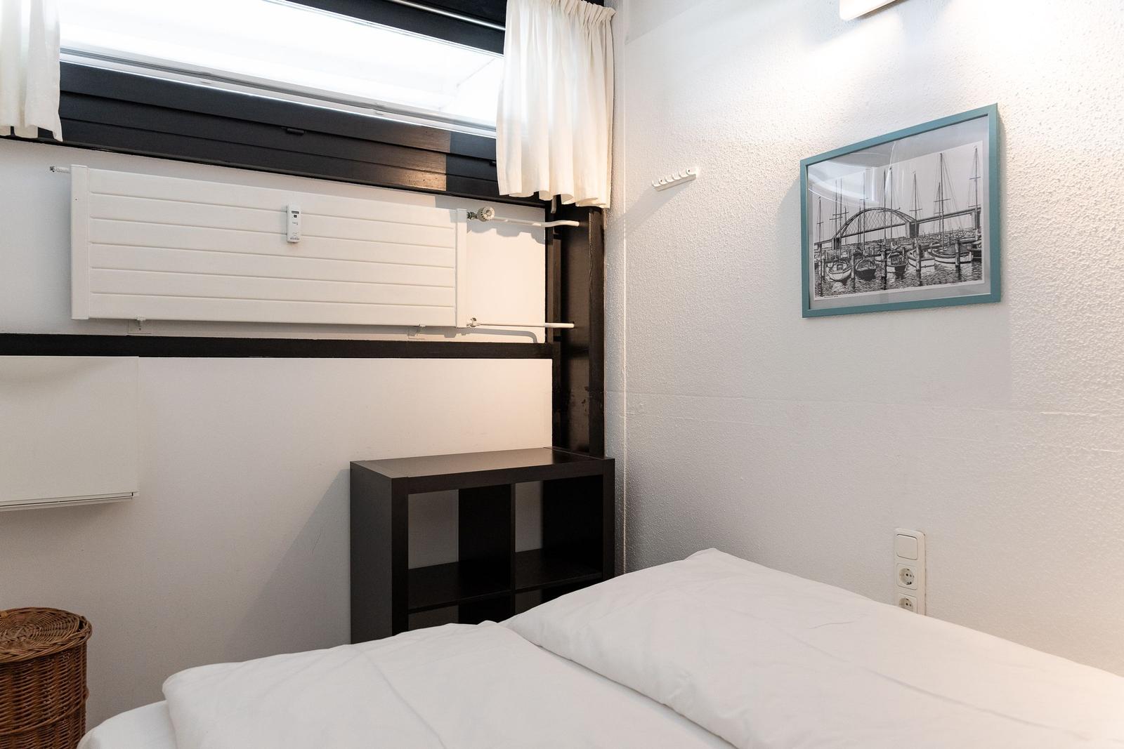 Schlafzimmer mit Bett, Wandbild, Schrank und Fenster mit Jalousie.