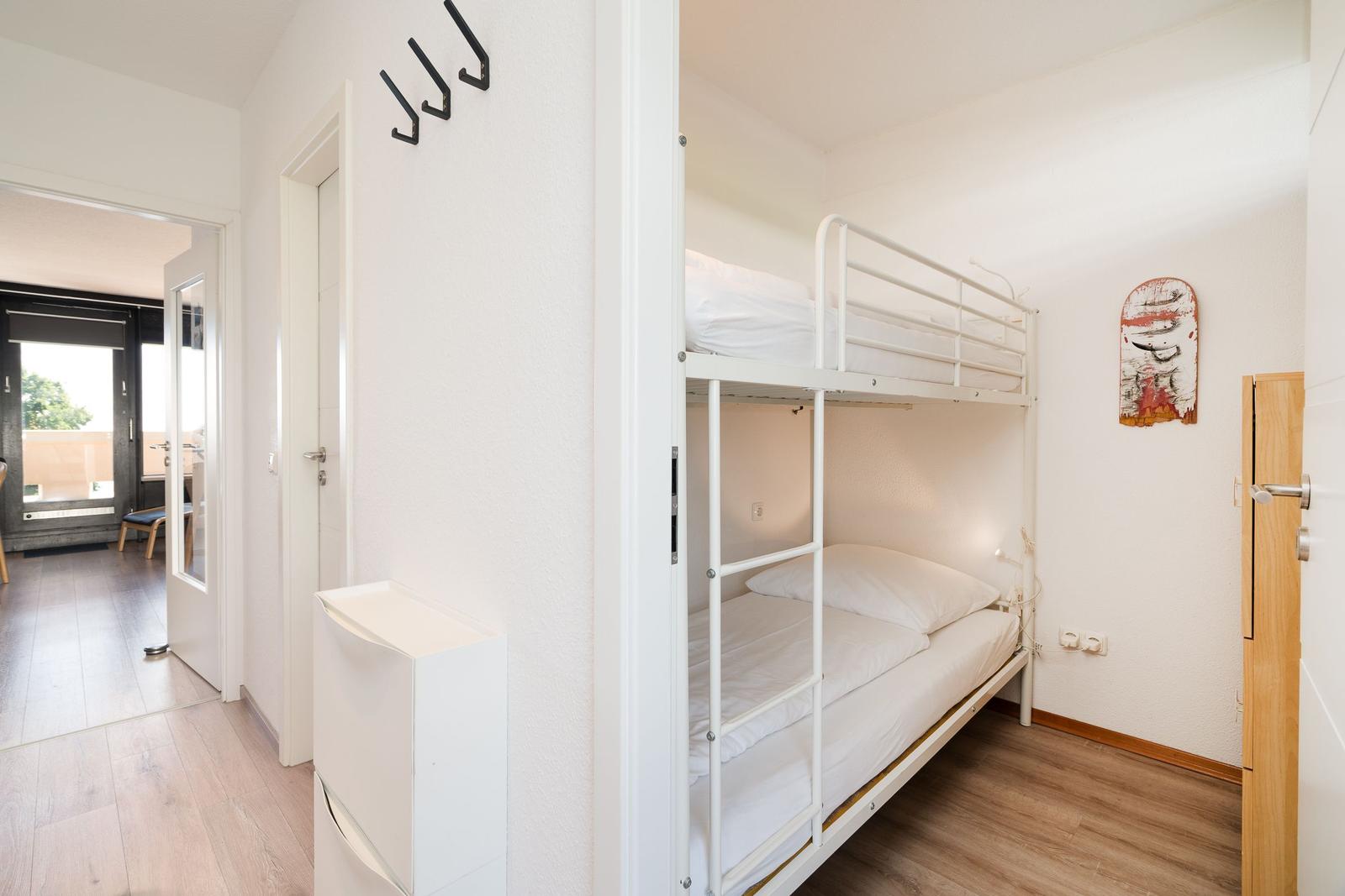 Zimmer mit Doppelstockbett, Holzboden und Wanddekoration. Tür führt zum Flur.