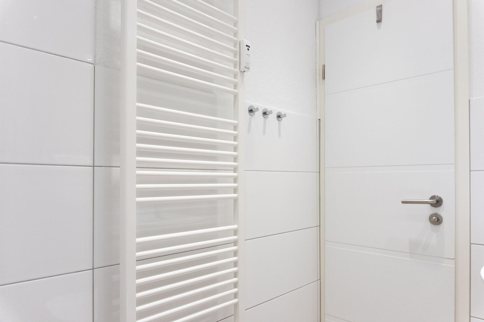 Wohnung mit weißen Fliesen, Heizkörper und Tür mit Metallgriff.