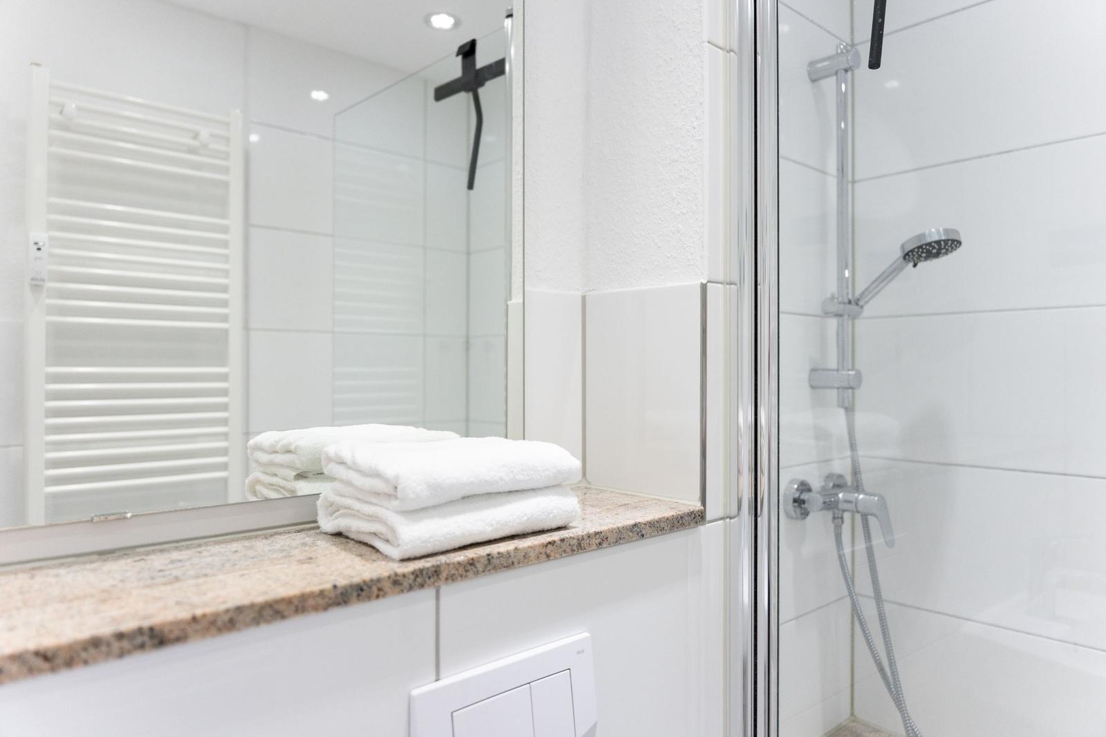 Badezimmer mit Dusche, Spiegel und Handtüchern auf Marmorarbeitsplatte.