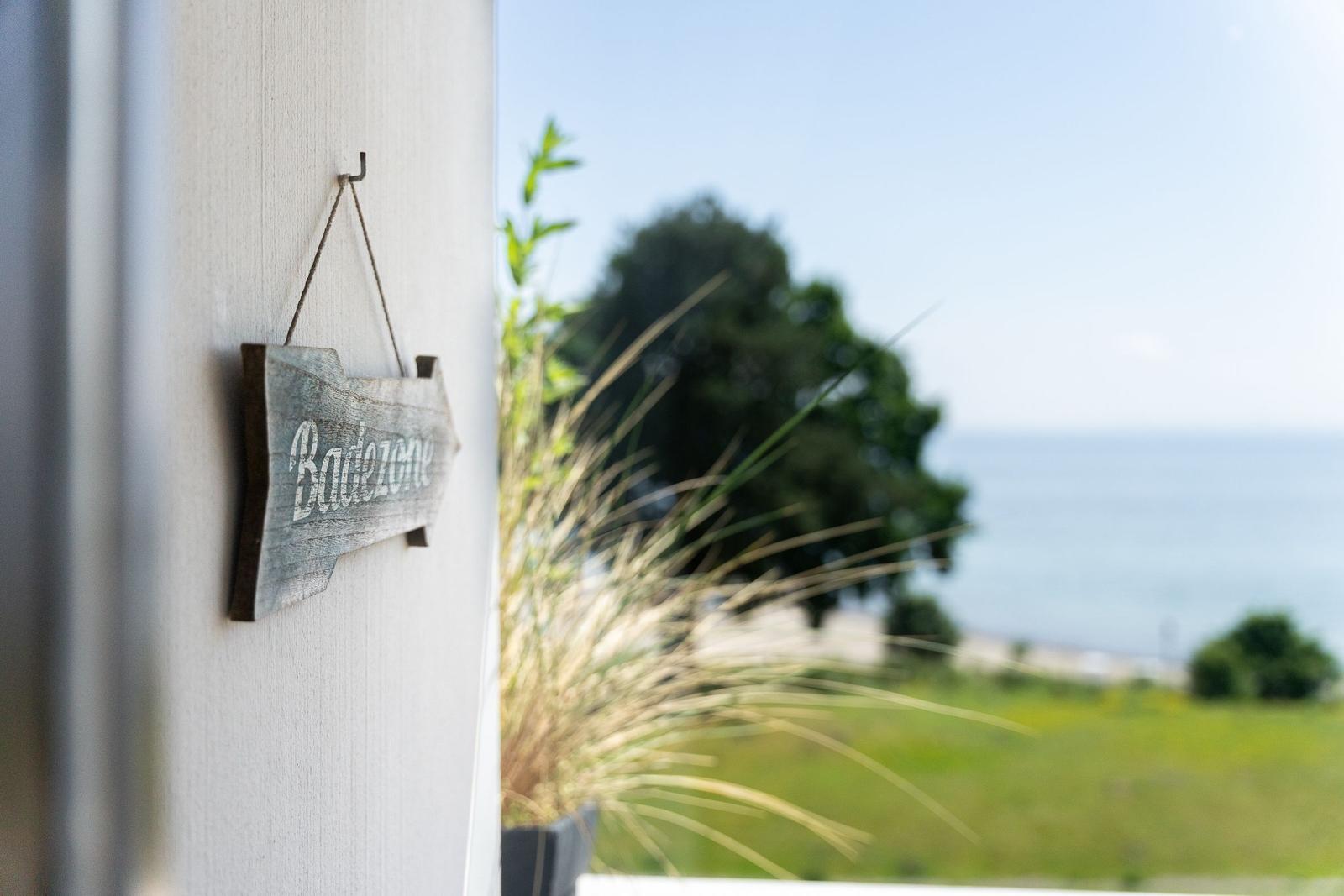 Schild zeigt Richtung Badestelle mit Blick auf Meer und Grünflächen.