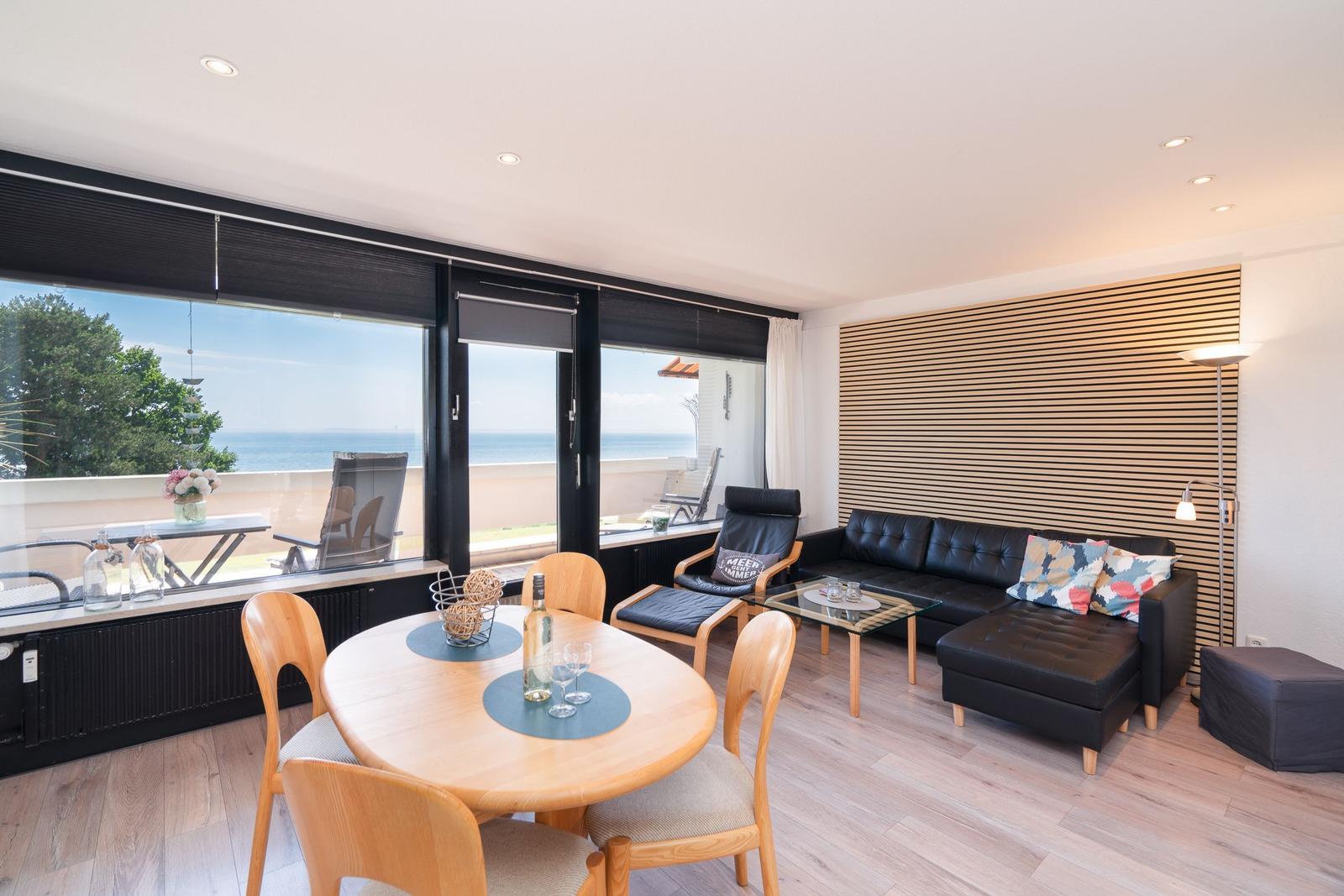Wohn- und Essbereich mit Blick aufs Meer. Schwarzes Sofa, Holztisch und Terrasse.