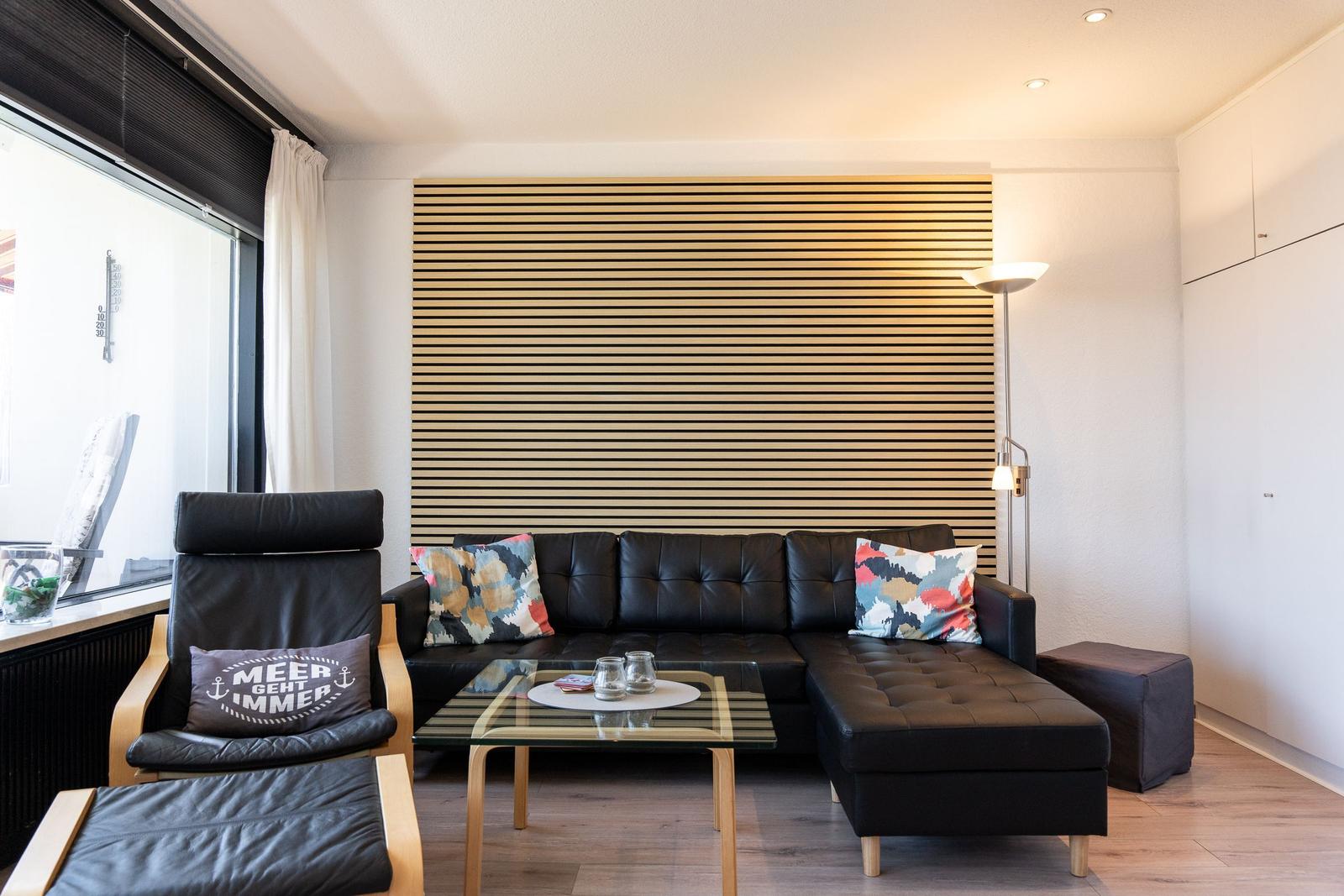 Schwarzes Sofa mit Kissen, Glas-Tisch und Holzwand im Wohnzimmer.