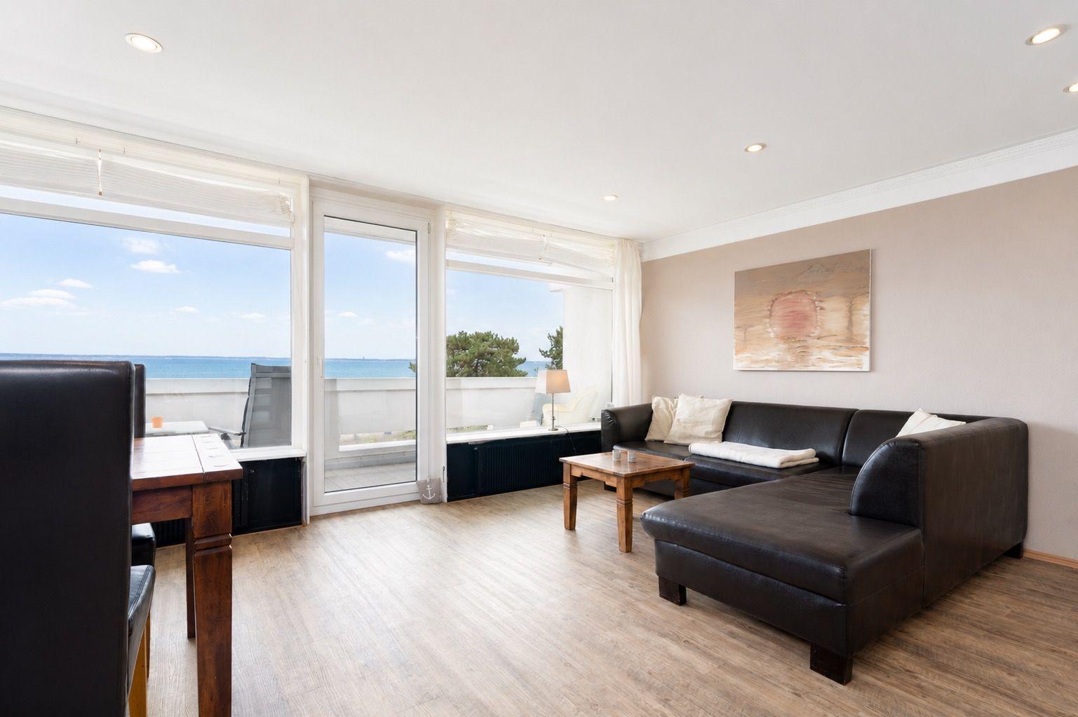 Wohnzimmer mit Sofa, Tisch und Meerblick durch große Fenster.