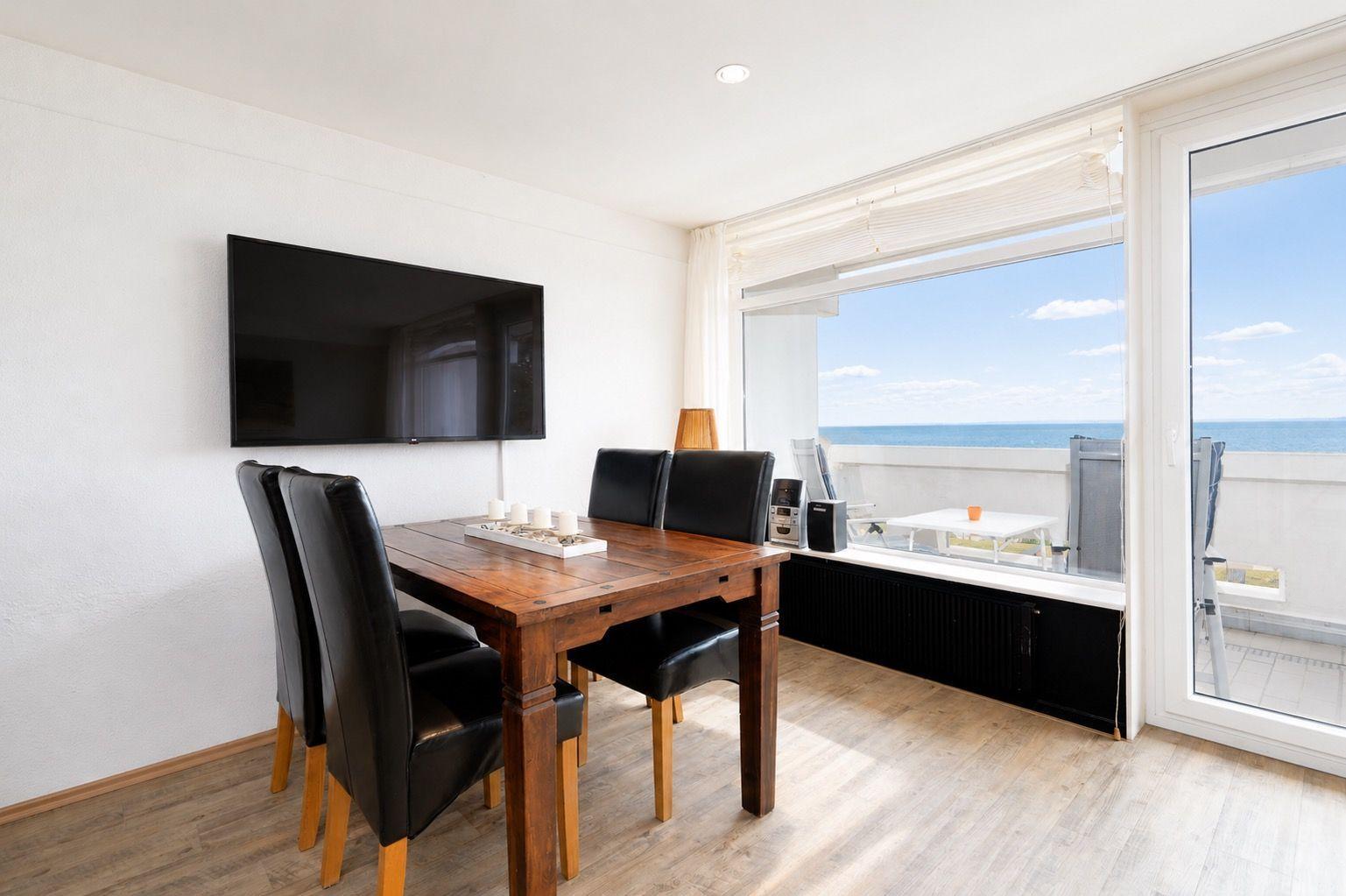 Esszimmer mit Tisch, Stühlen und TV. Blick aufs Meer vom Balkon.