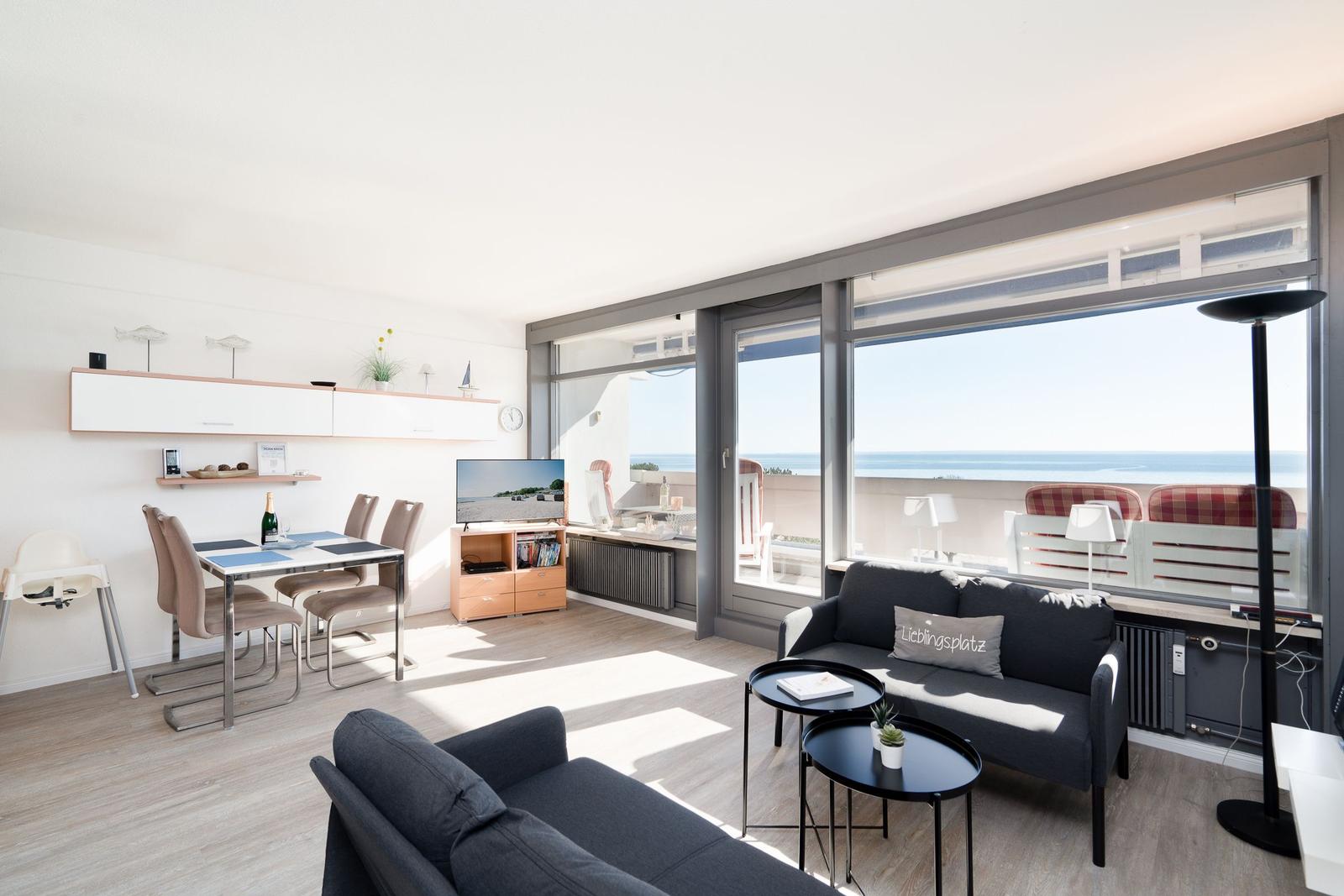 Wohnbereich mit Sofa, Esstisch und großem Fenster zum Meer.