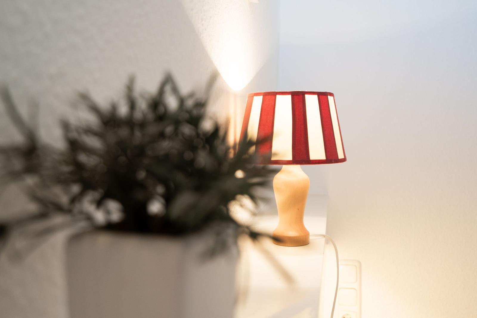 Eine Lampe mit rot-weißem Schirm steht auf einem Tisch neben einer Pflanze.