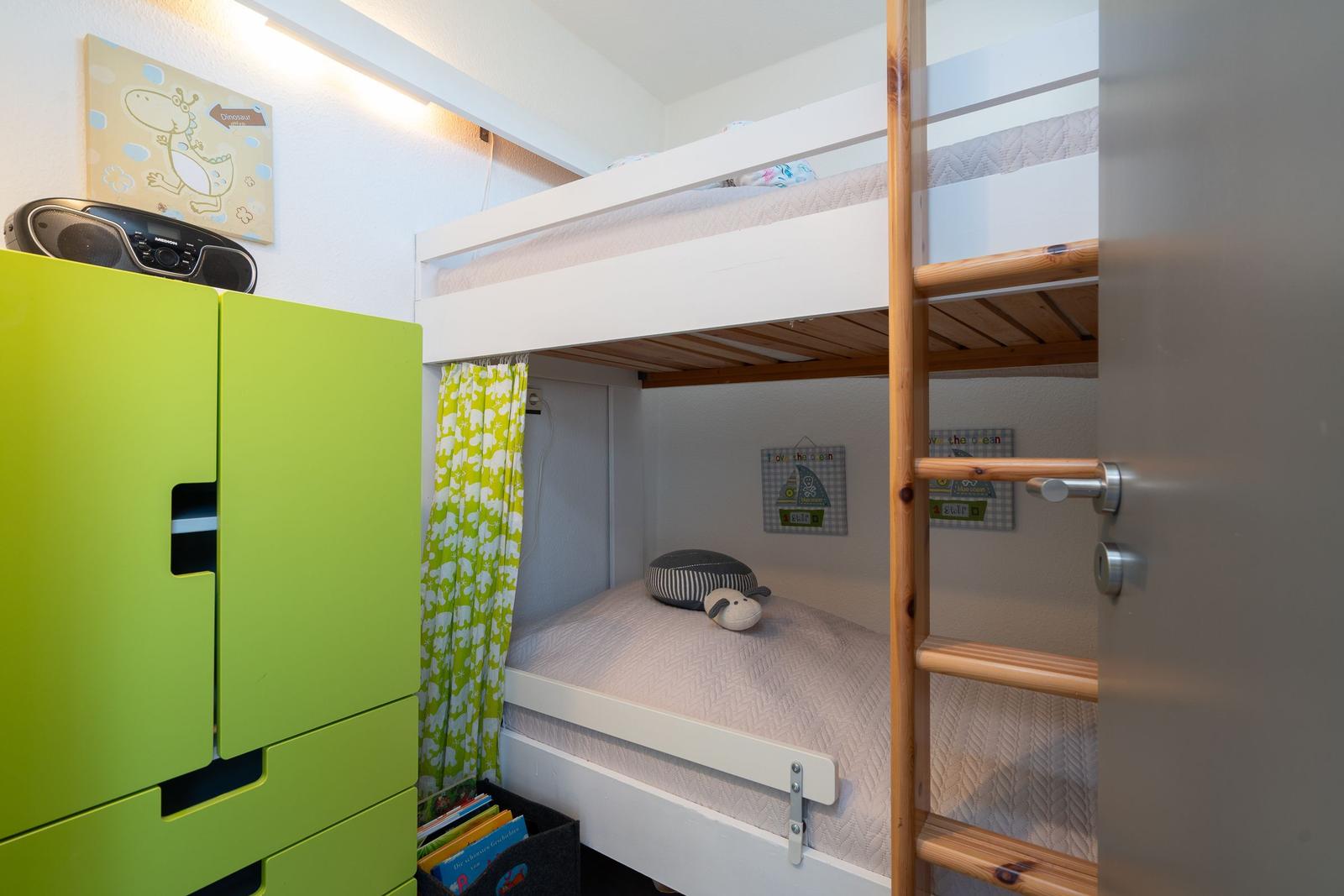 Ein Schlafzimmer mit Doppelstockbett, grünem Schrank und Vorhang.
