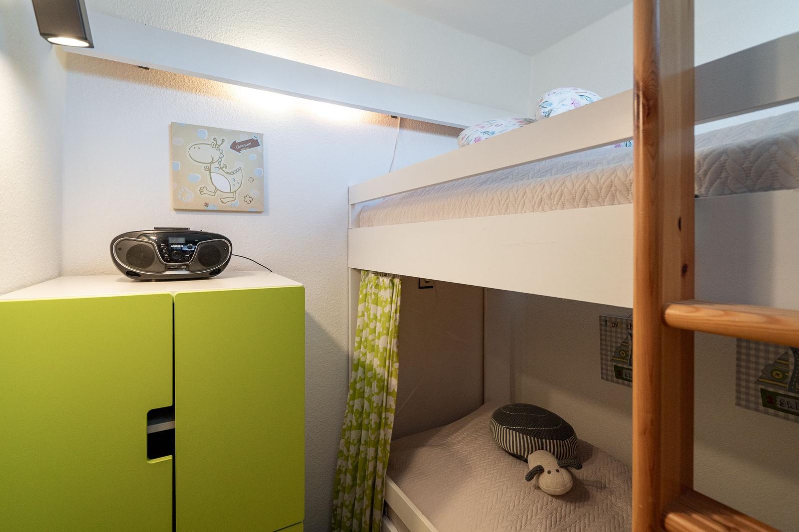Ein Schlafzimmer mit Doppelstockbett, grünem Schrank und Wandbild mit Dinosaurier.