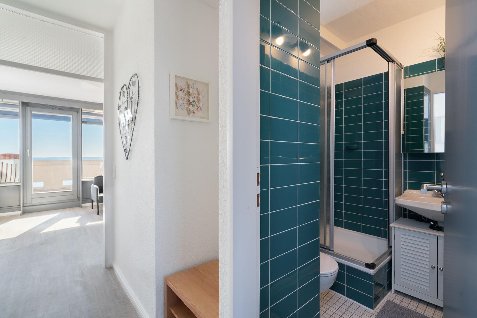 Badezimmer mit Dusche und Waschbecken. Blick auf Balkon mit Meerblick.