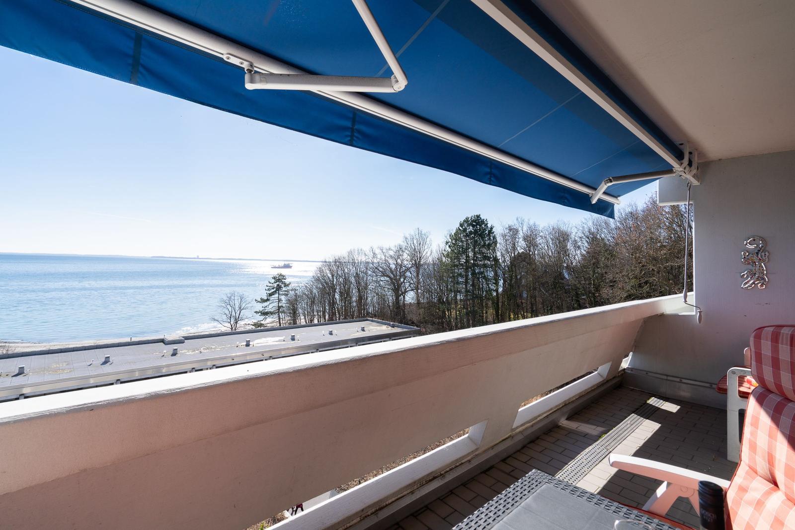 Terrasse mit Blick auf Meer und Bäume unter blauem Markisen.