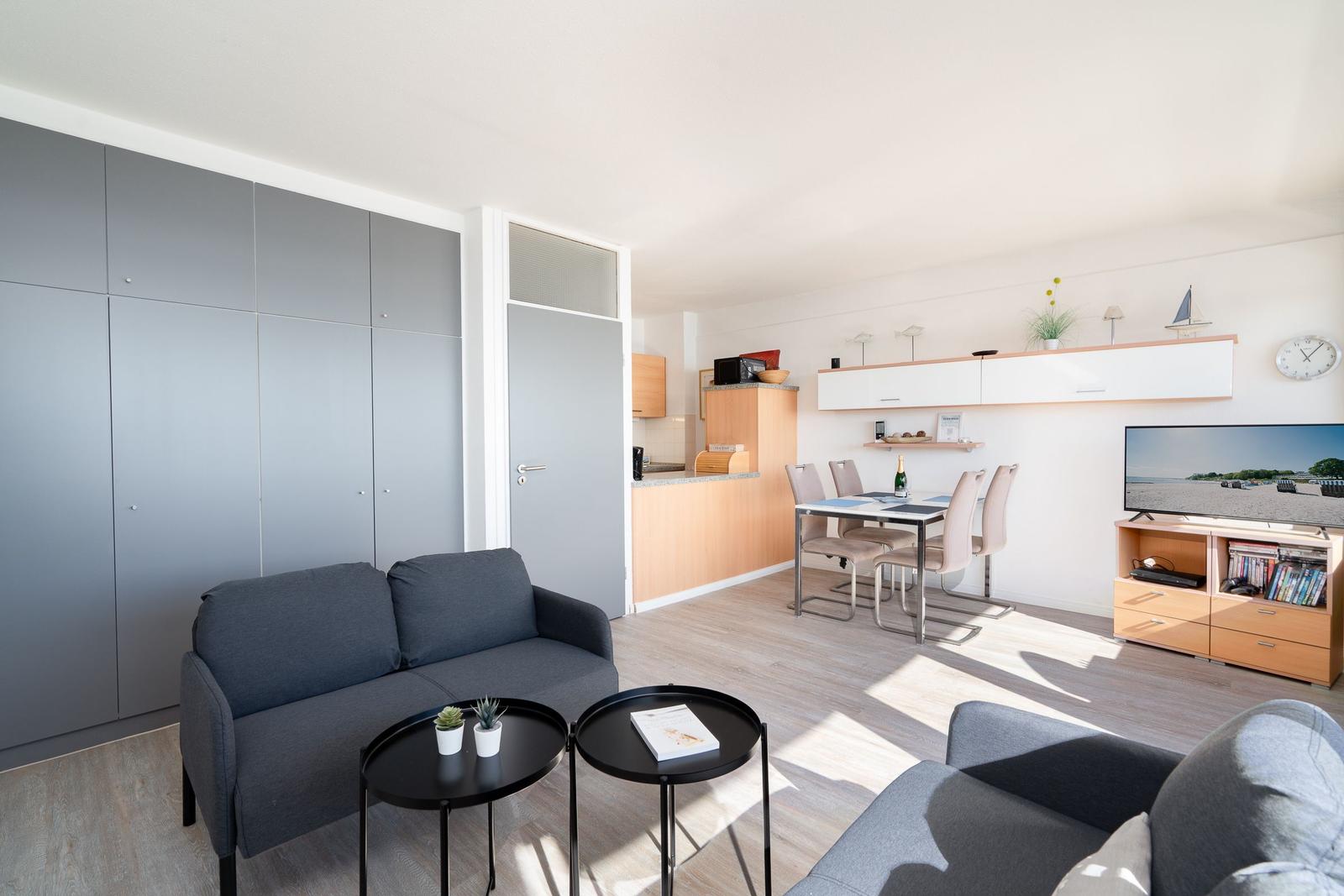 Wohnbereich mit Sofa, Esstisch und TV. Küche im Hintergrund.