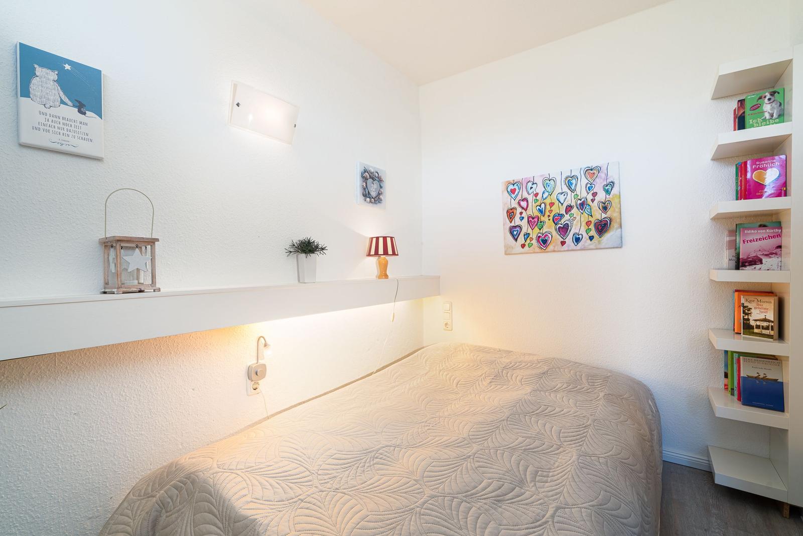 Ein Schlafzimmer mit Bett, Wandregal und Wandbildern.