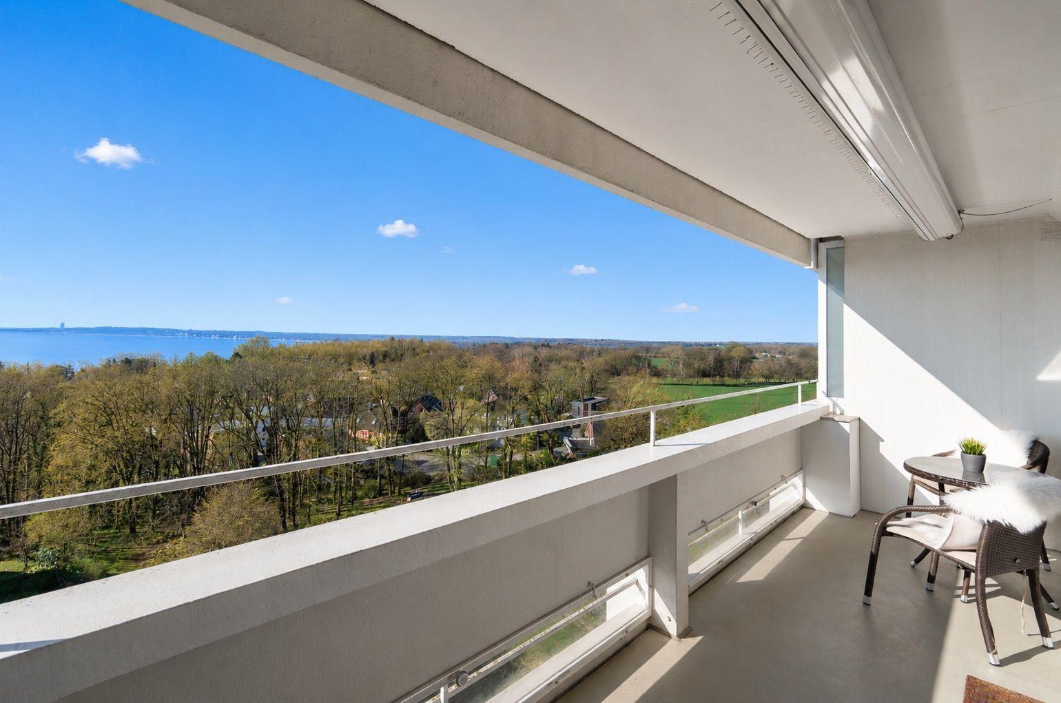 Terrace with view of lake and forests. Table, chairs, and plant are present.