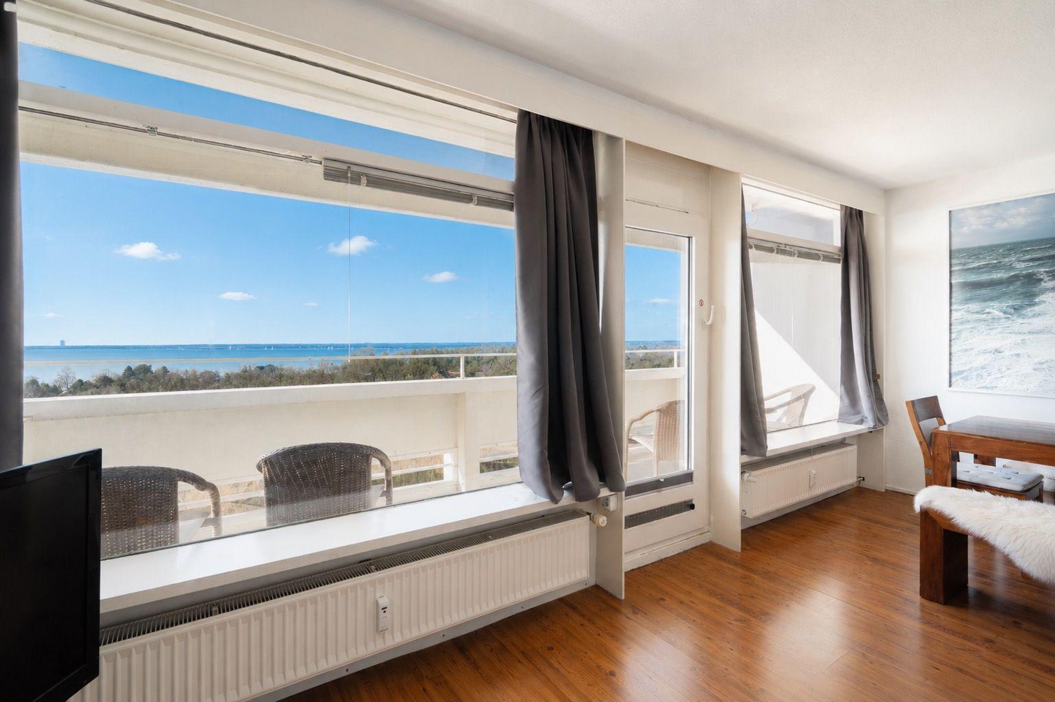 Room with sea view, balcony, wooden floor, and wall art.