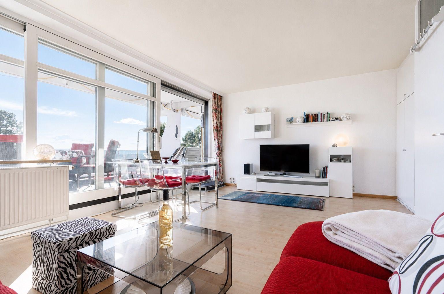 Living room with glass patio, red sofa, and TV wall. Terrace with sea view.