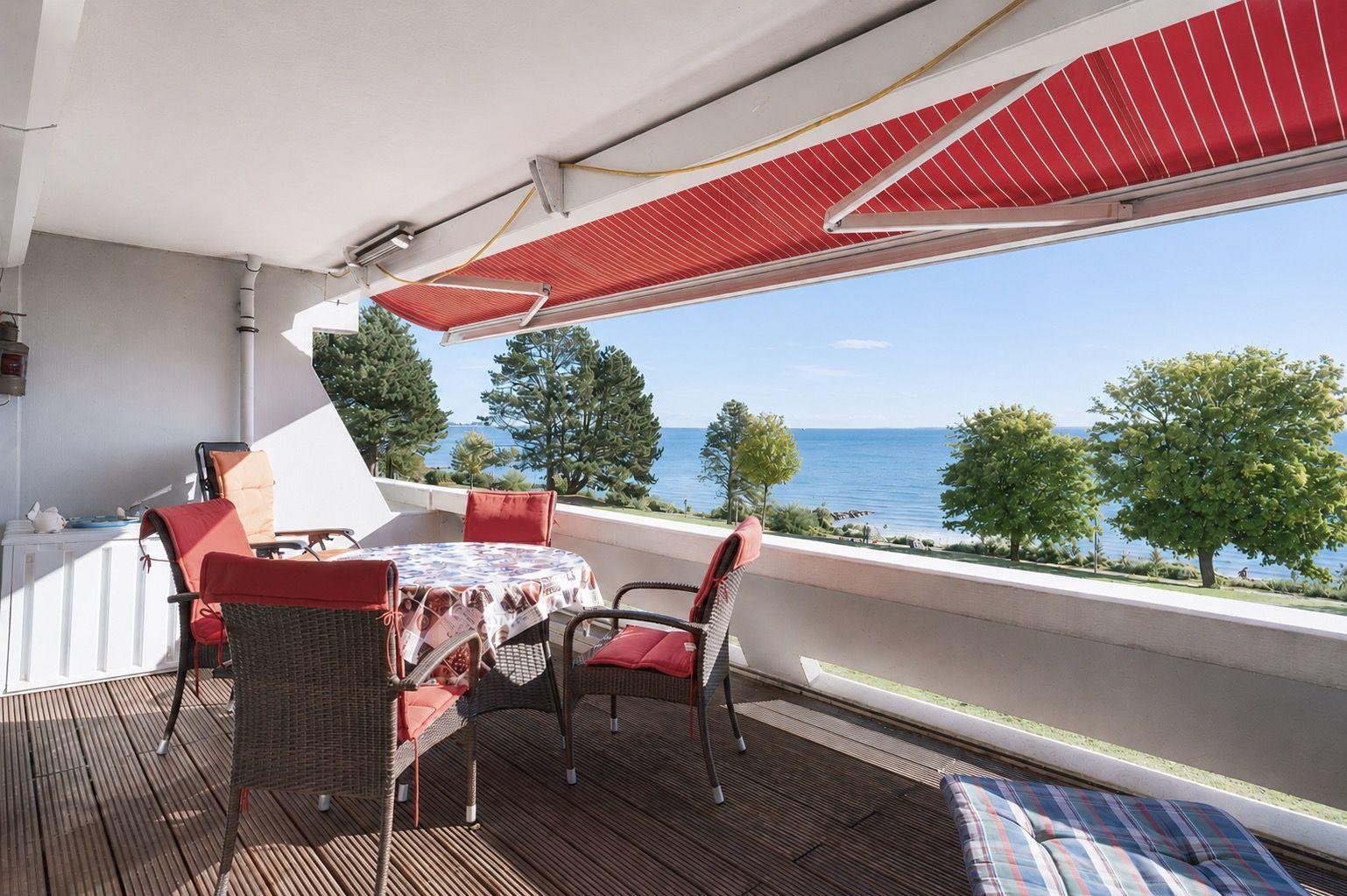 Terrace with table, chairs, and view of sea and trees.