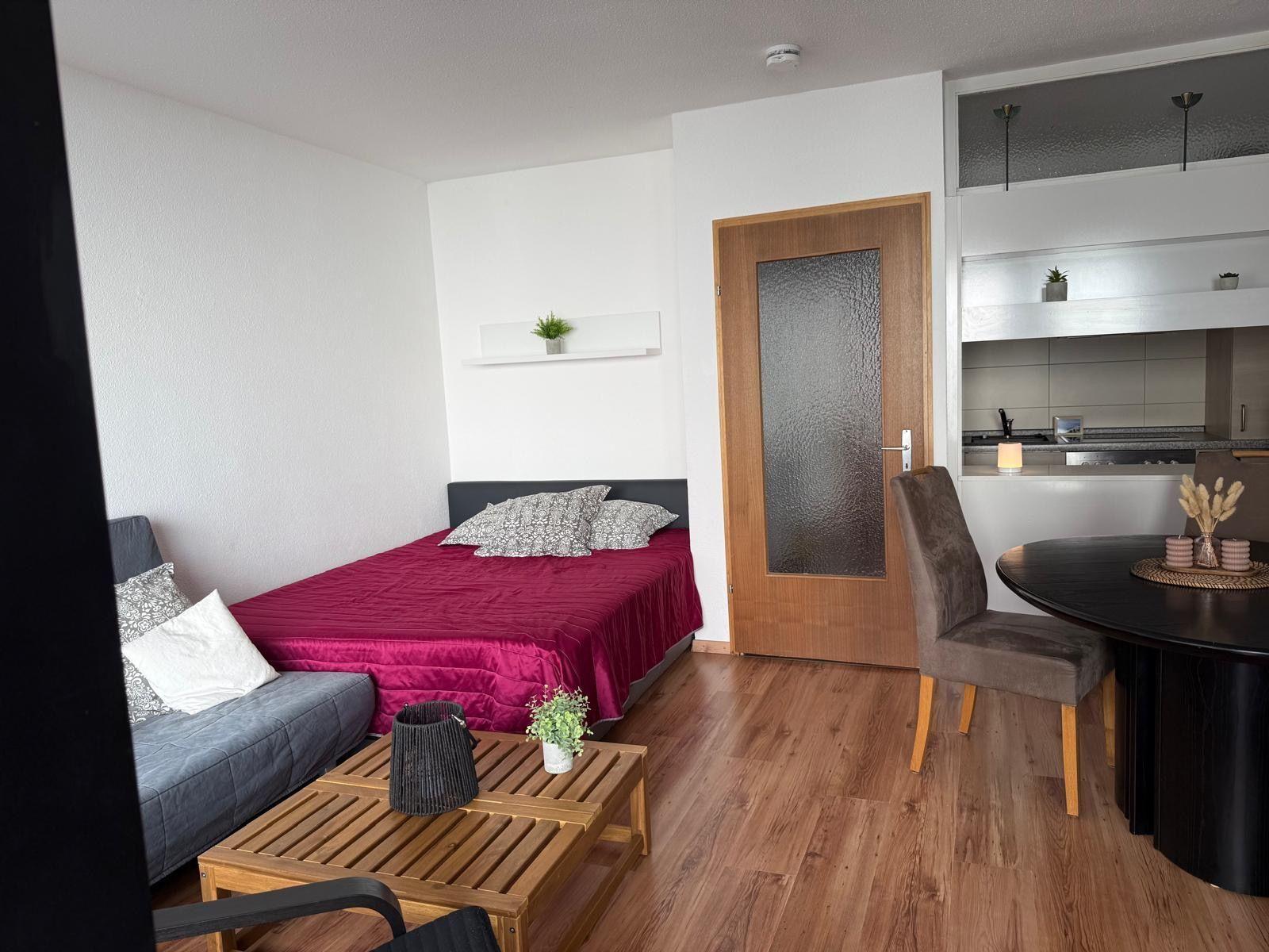 Schlafzimmer mit Bett, Couch und Küchenbereich im Hintergrund.