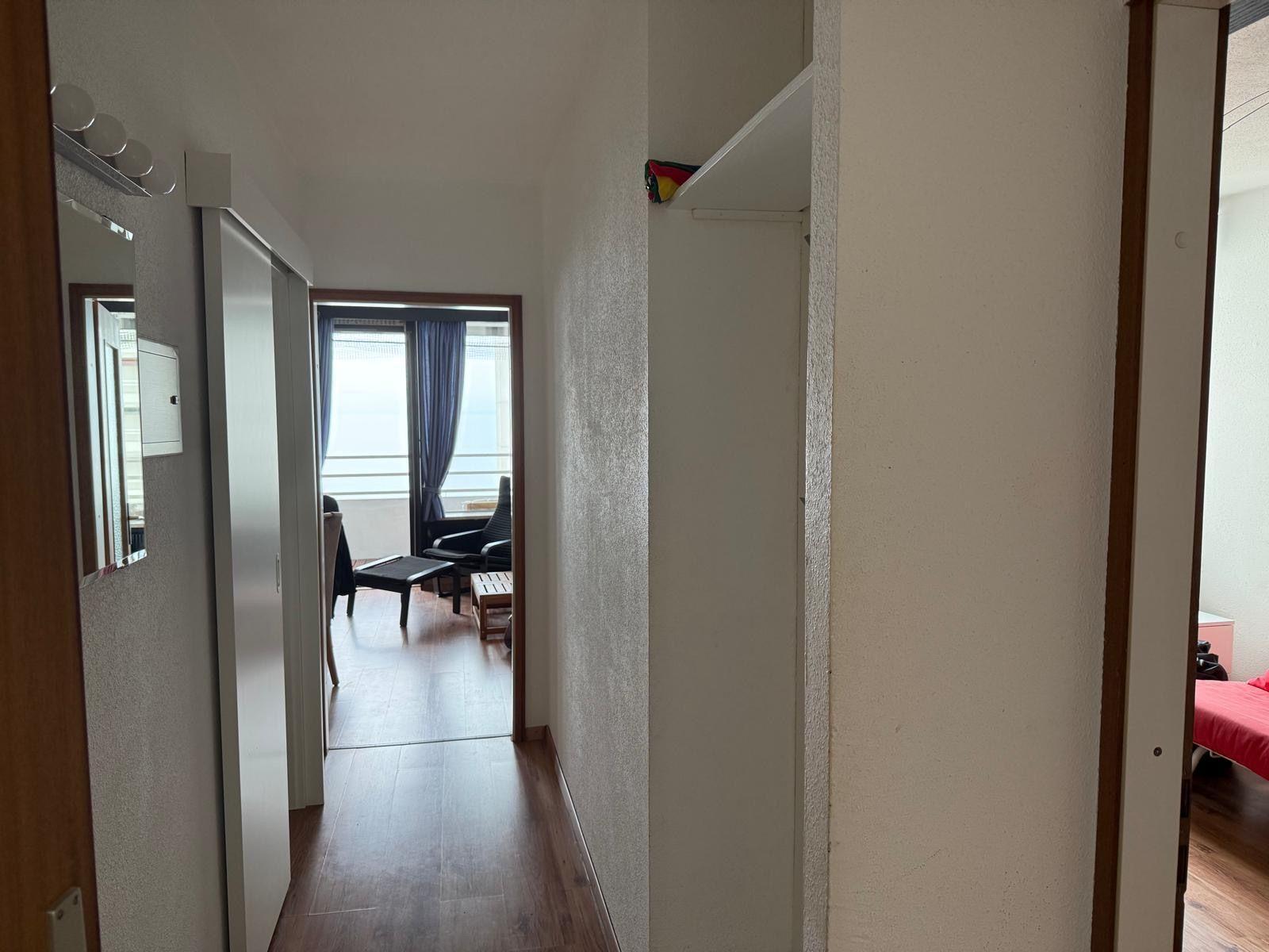 Flur mit Blick in Wohnbereich und Schlafzimmer mit rotem Bett.