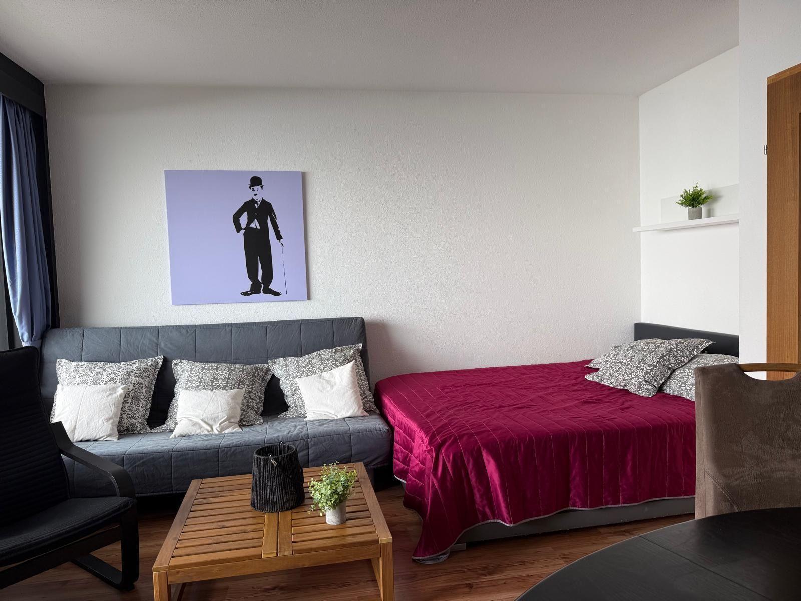 Zimmer mit Sofa, Bett und Wandbild von Charlie Chaplin.