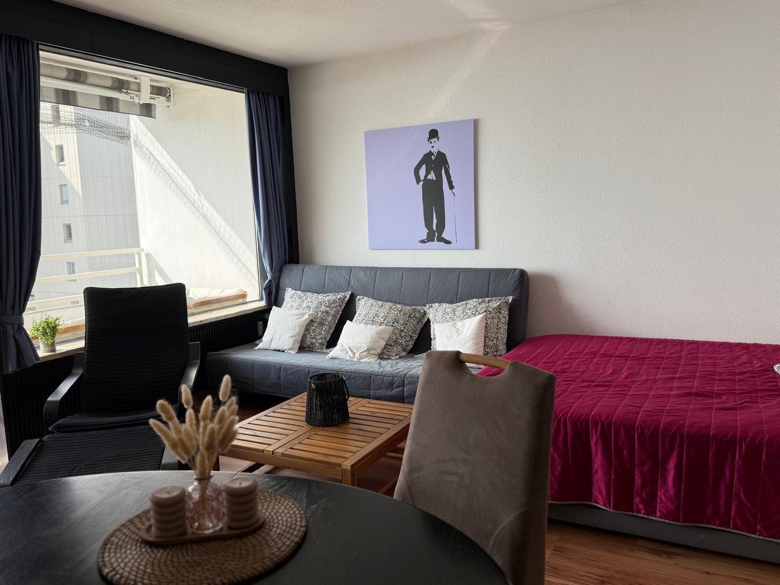 Zimmer mit Sofa, Bett und Tisch. An der Wand hängt ein Bild von Charlie Chaplin.