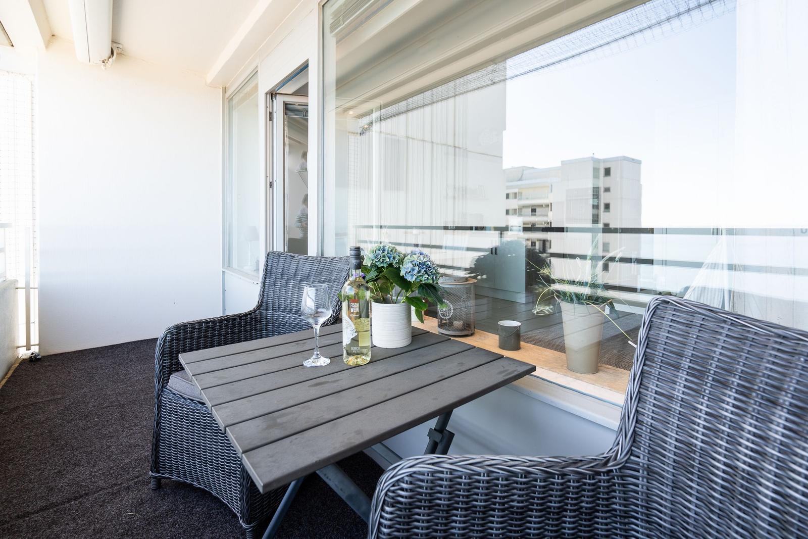 Balcony with table, two chairs, plants, and a wine bottle.