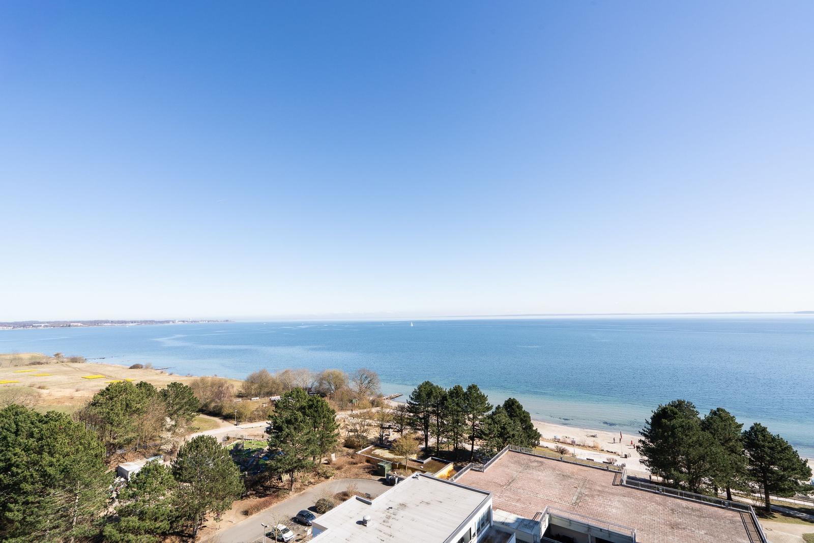 Panoramic view of the sea and beach with trees and buildings in the foreground.