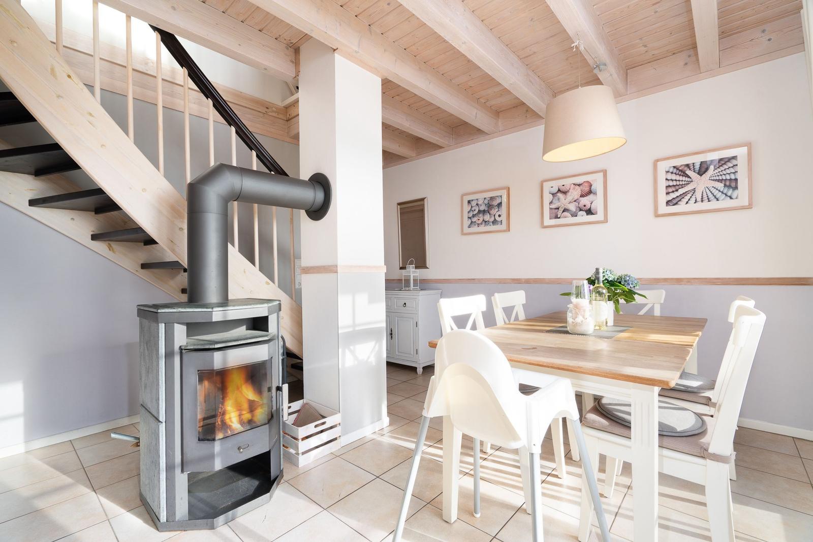 Esszimmer mit Holztisch, weißen Stühlen und Kaminofen. Holzdecke und Wandbilder mit Muscheln.
