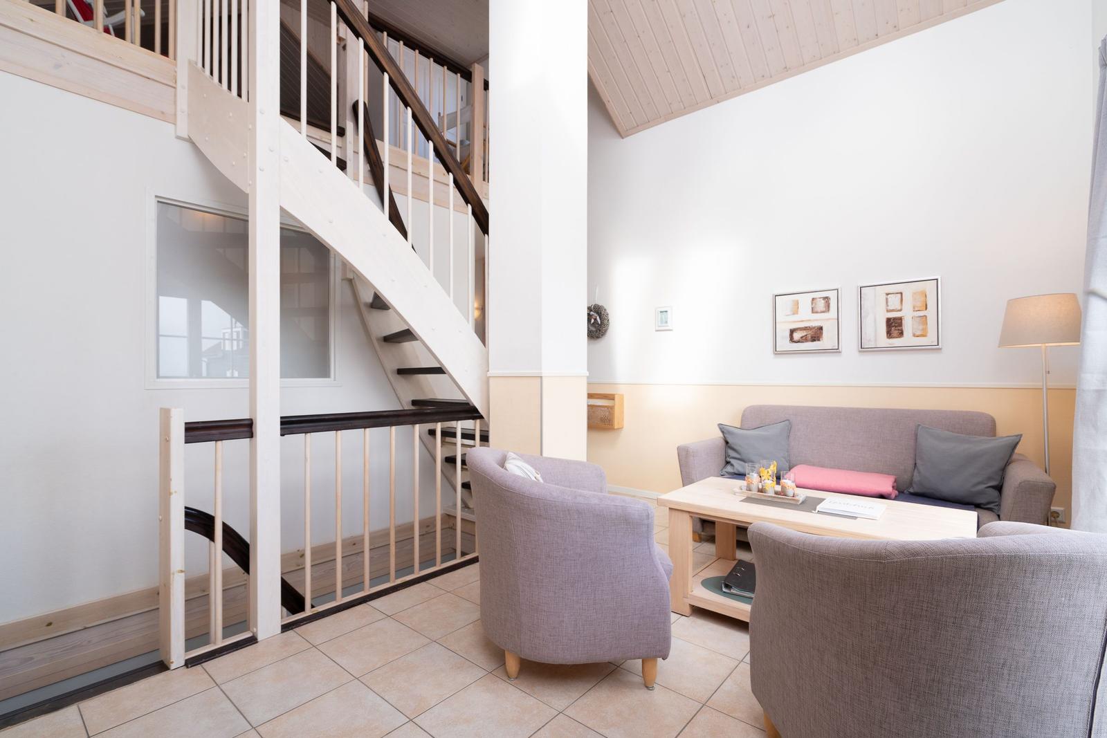 Wohnbereich mit Sofa, zwei Sesseln und Treppe zur oberen Etage.