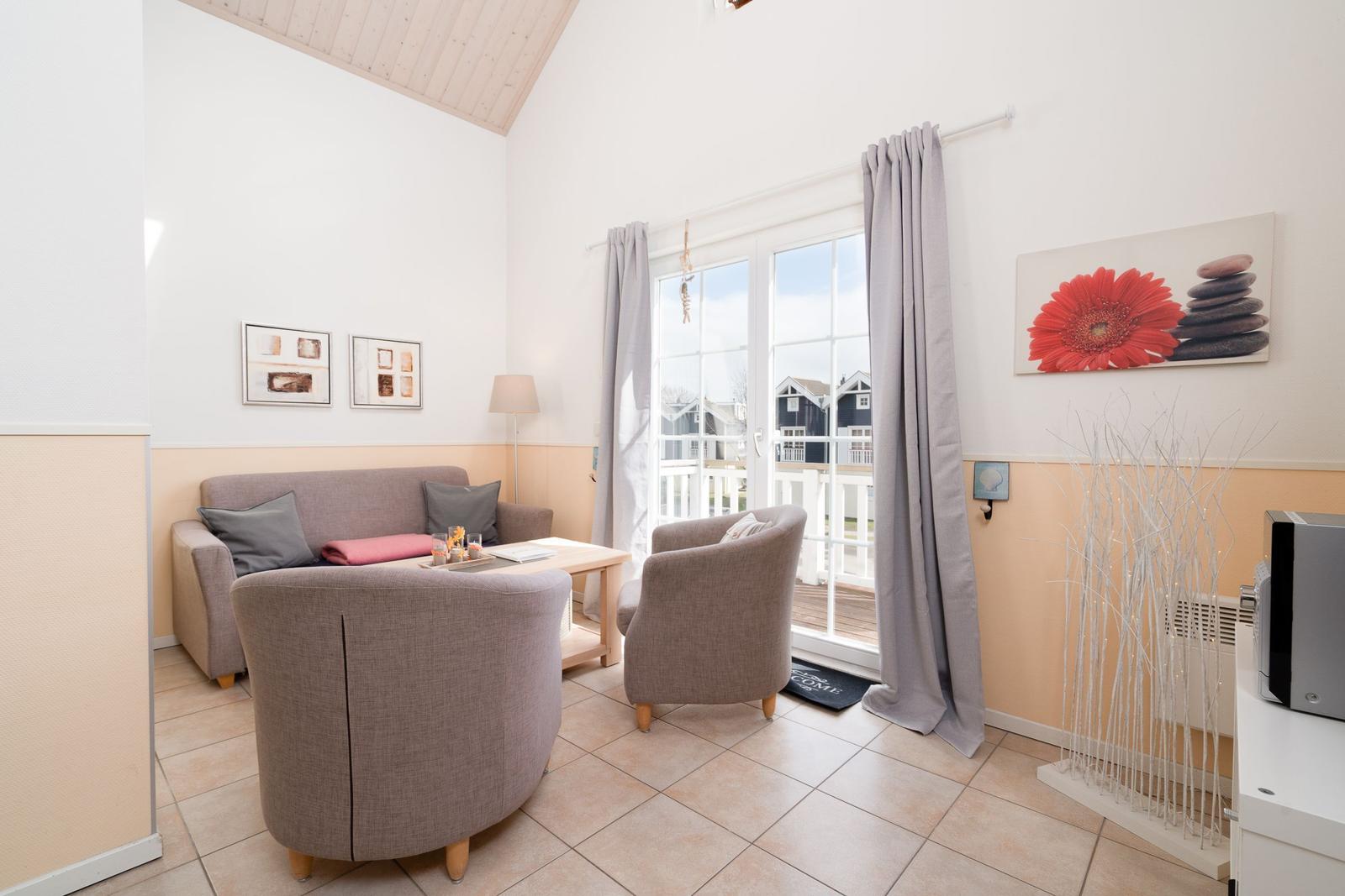 Wohnzimmer mit Sofa, zwei Sesseln und Blick auf Balkon. Wandbild mit Blume und Steinen.