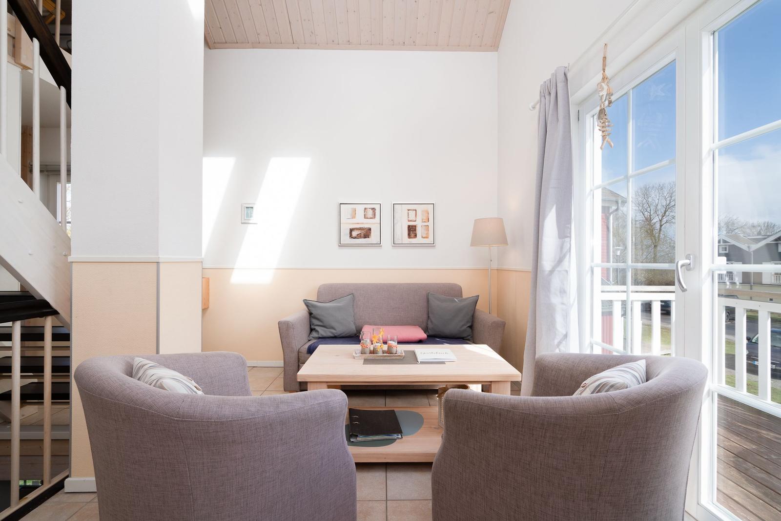 Wohnzimmer mit Sofa, zwei Sesseln und Tisch. Durchgang zur Terrasse mit Blick nach draußen.