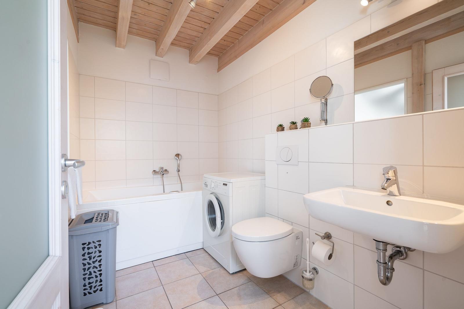 Badezimmer mit Badewanne, Waschmaschine und WC. Holzdecke und weiße Fliesen.
