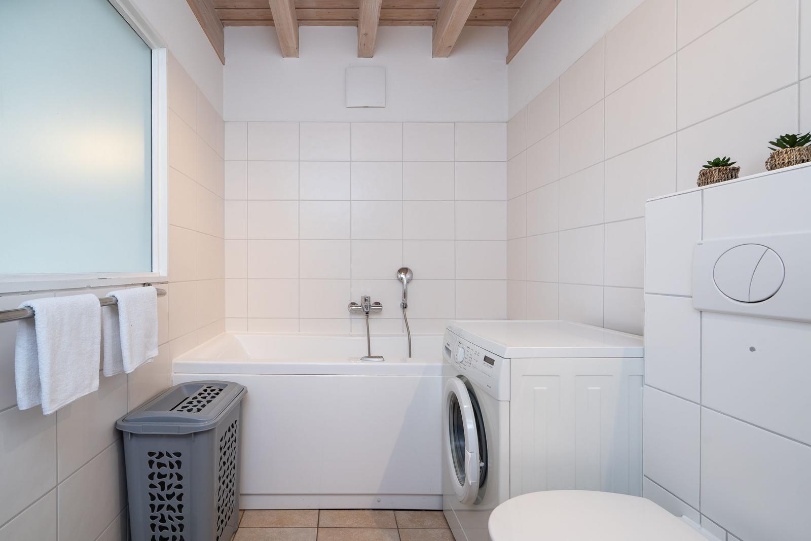 Badezimmer mit Badewanne, Waschmaschine und Toilette. Holzbalken an der Decke.