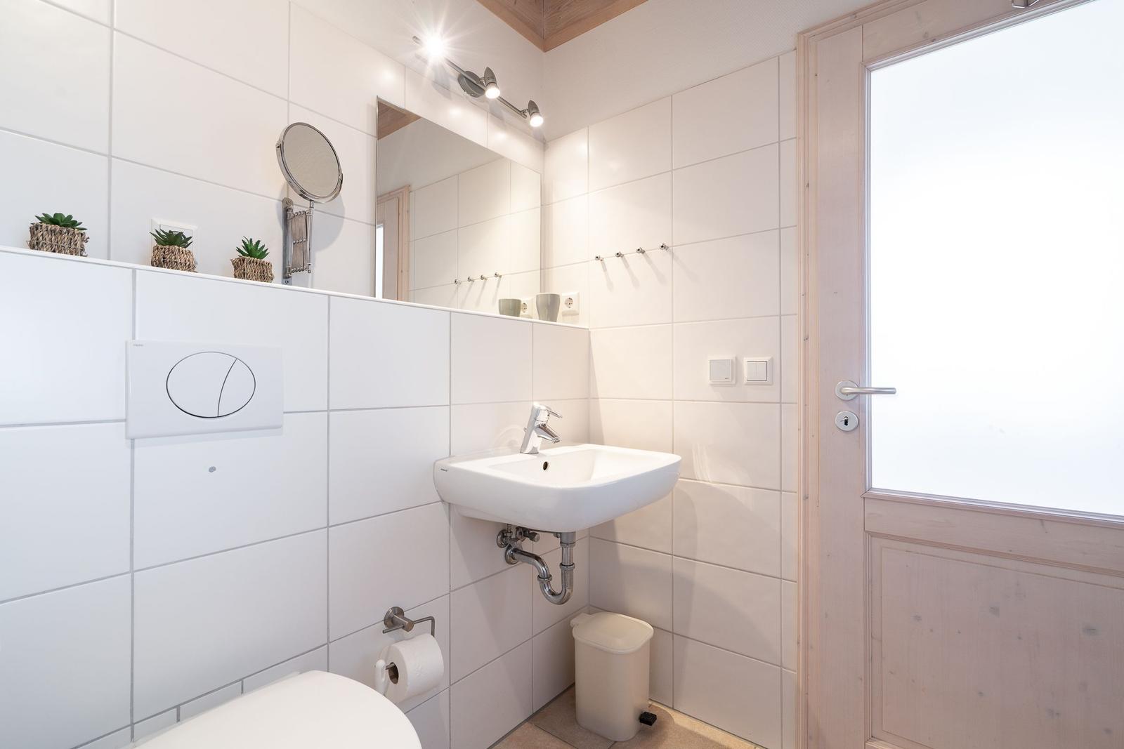 Badezimmer mit Waschbecken, Spiegel, Toilette und Fenster.